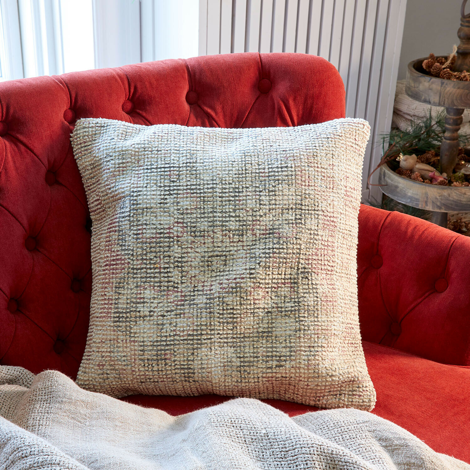 Beige decoratief kussen van zacht materiaal op rode gestoffeerde bank in lichte woonkamer