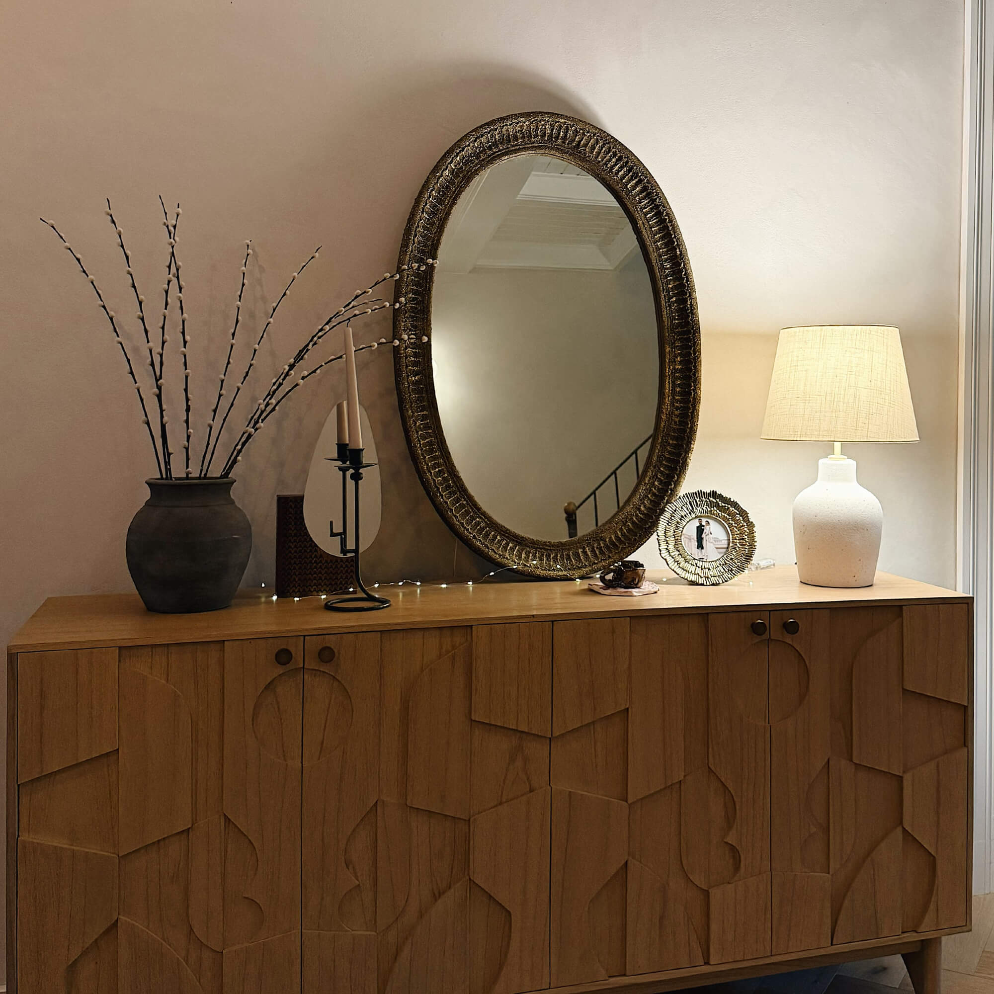 Houten dressoir met geometrisch patroon, ovale spiegel en lichte tafellamp in stijlvolle kamer