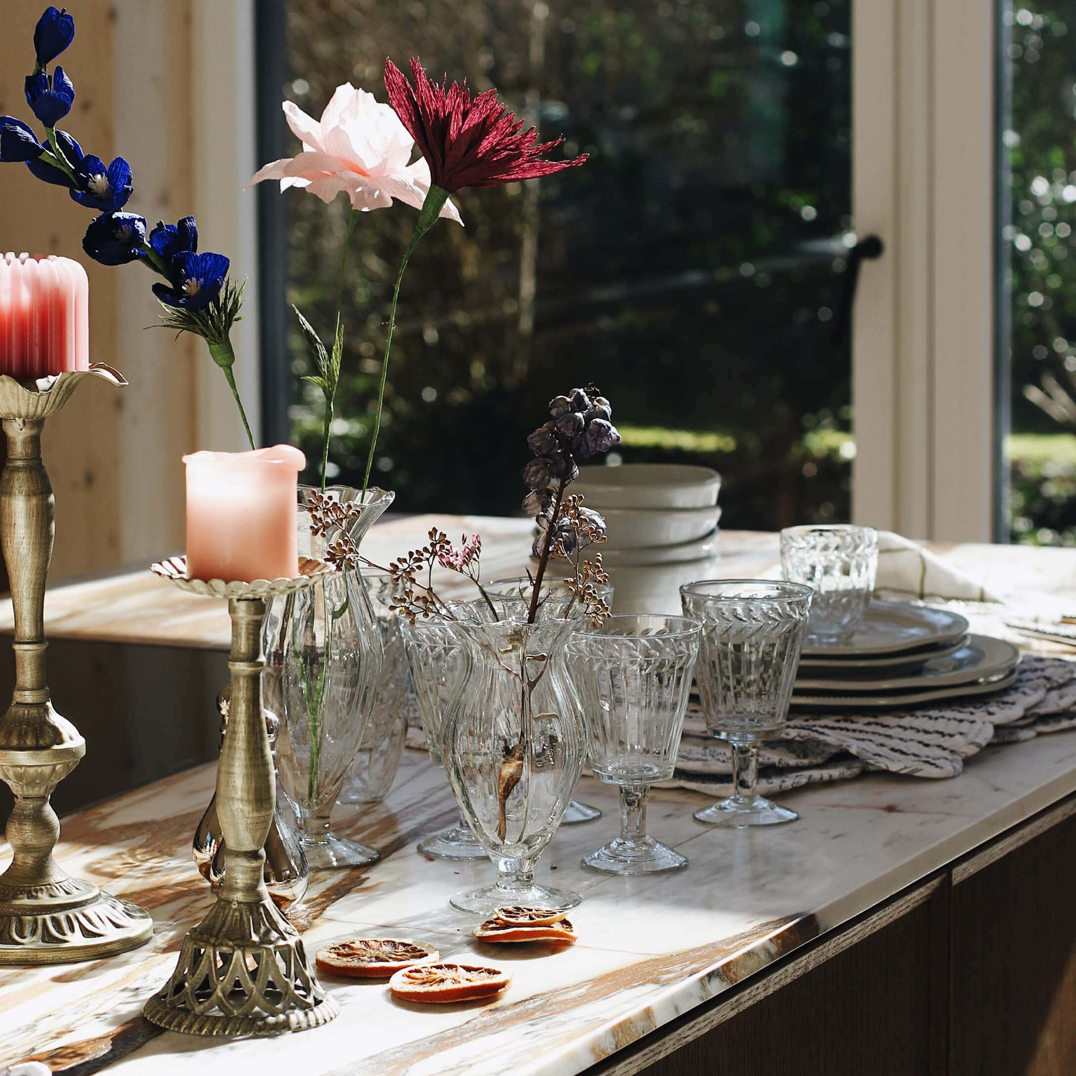 Glazen vazen en glazen op marmeren blad met gedroogde bloemen en decoratieve kaarsen