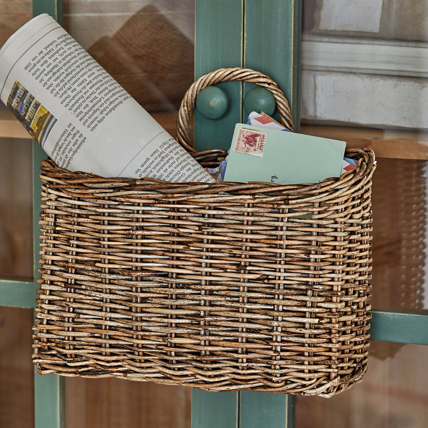 Natuurlijke rieten mand voor post en kranten aan groene deur gehangen