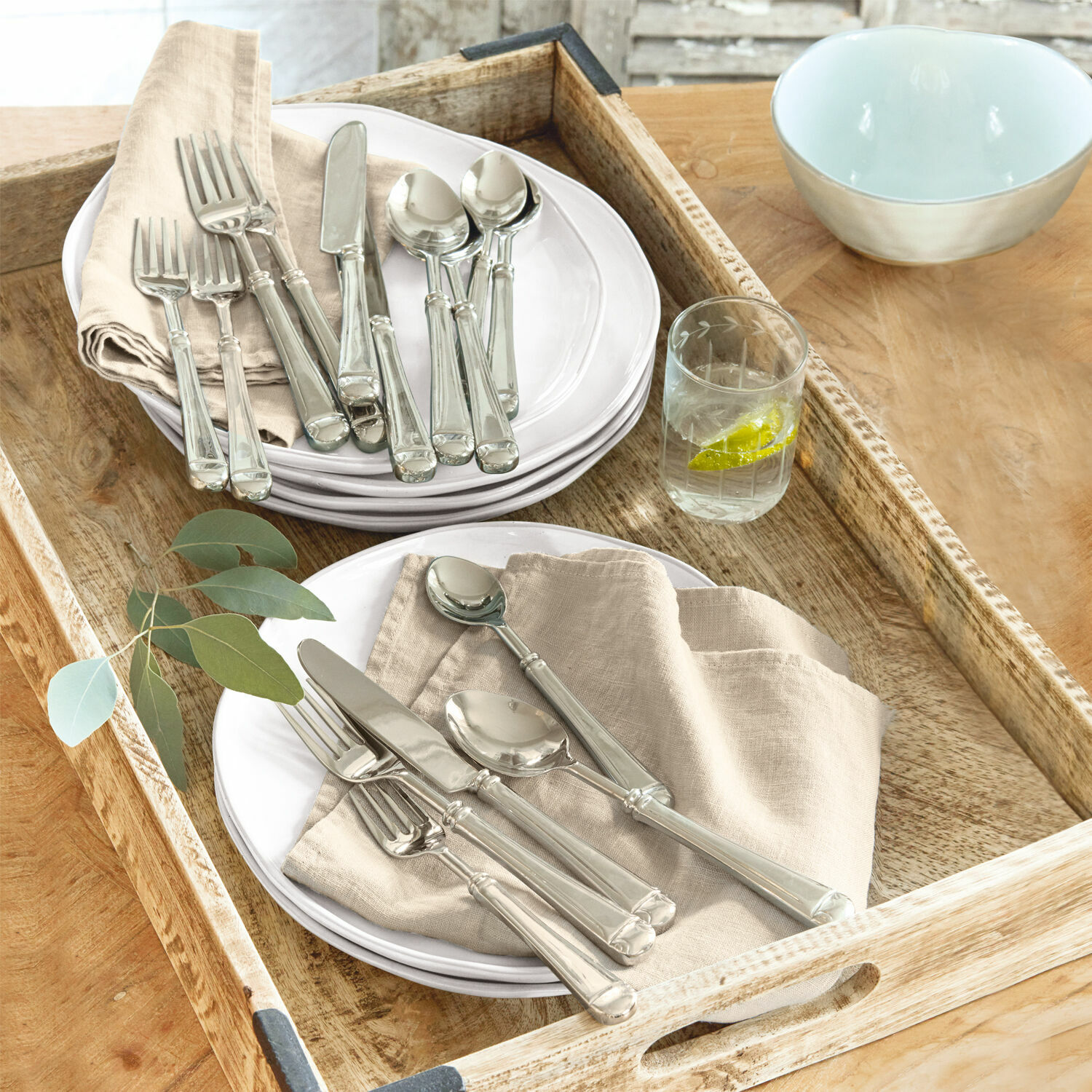 Bestek Eriat Set zilveren bestek op witte borden met beige servetten op houten dienblad