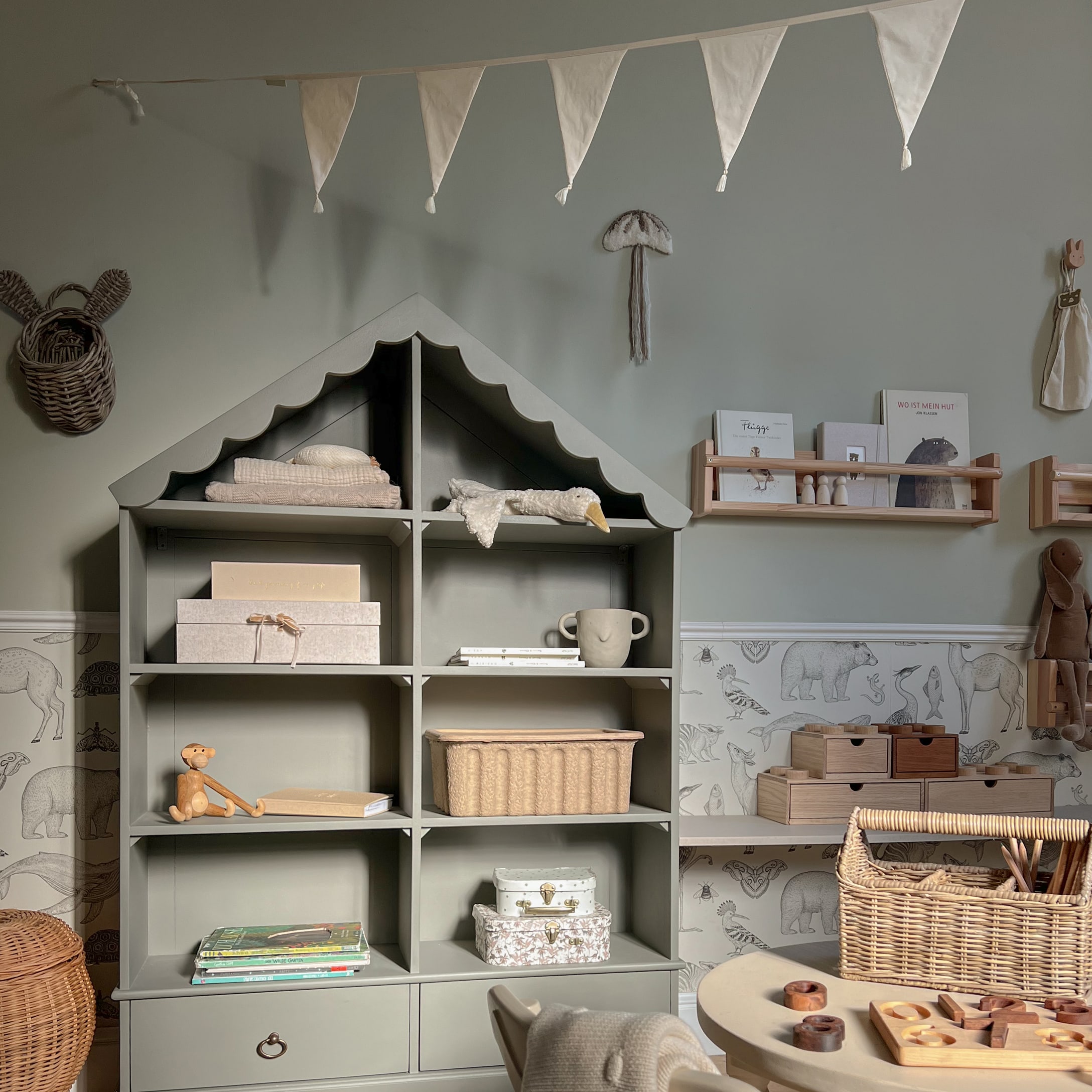 Grijze houten kast in huisvorm met decoraties en speelgoed in kinderkamer