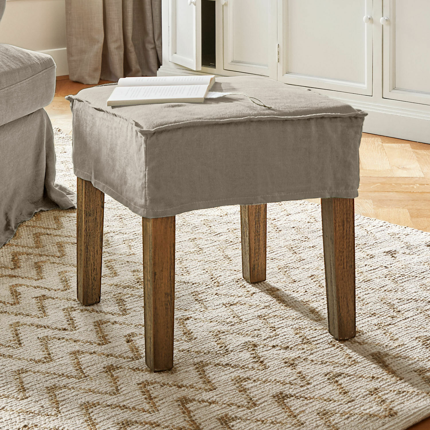Kruk Vionnique Beige poef met katoenen hoes en houten poten op lichte vloerkleed in woonkamer