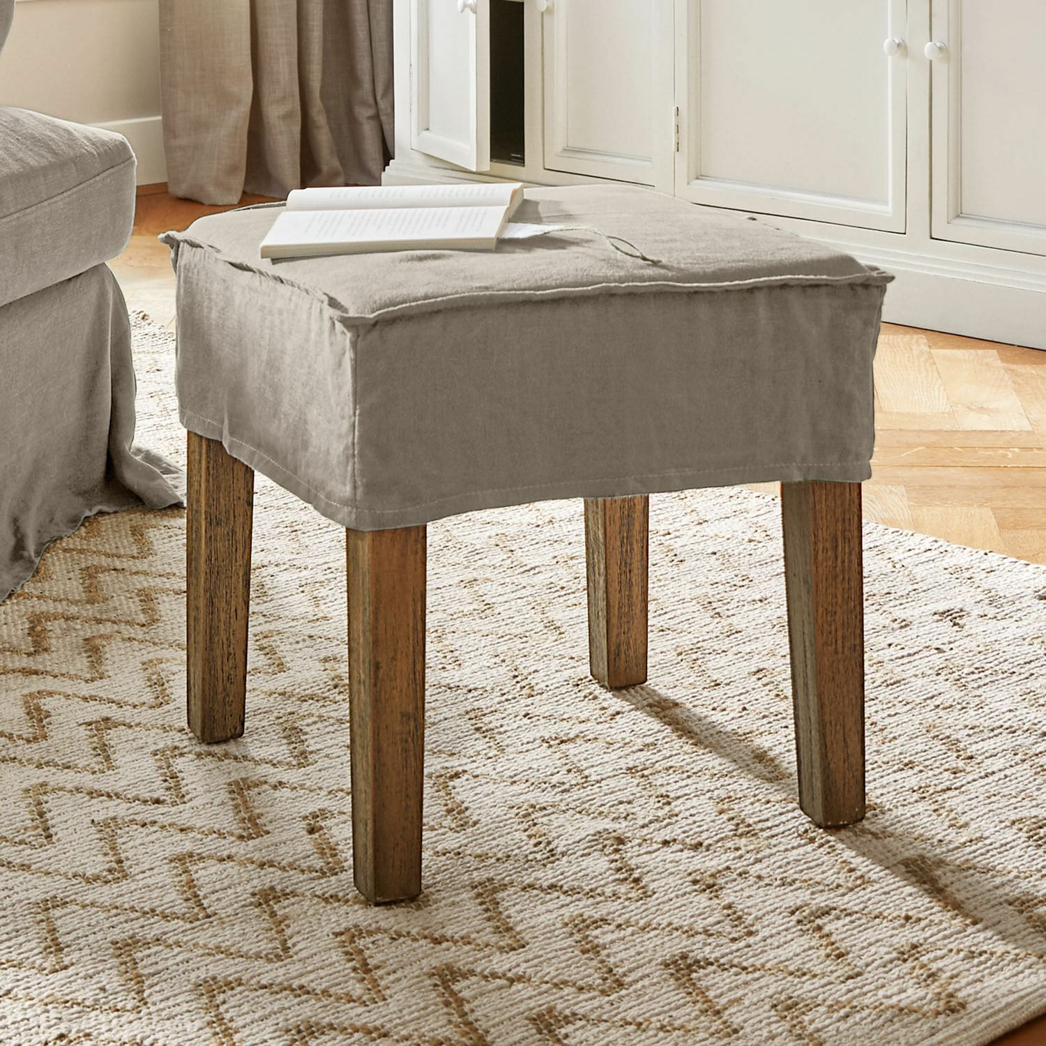 Kruk Vionnique Beige poef met katoenen hoes en houten poten op lichte vloerkleed in woonkamer