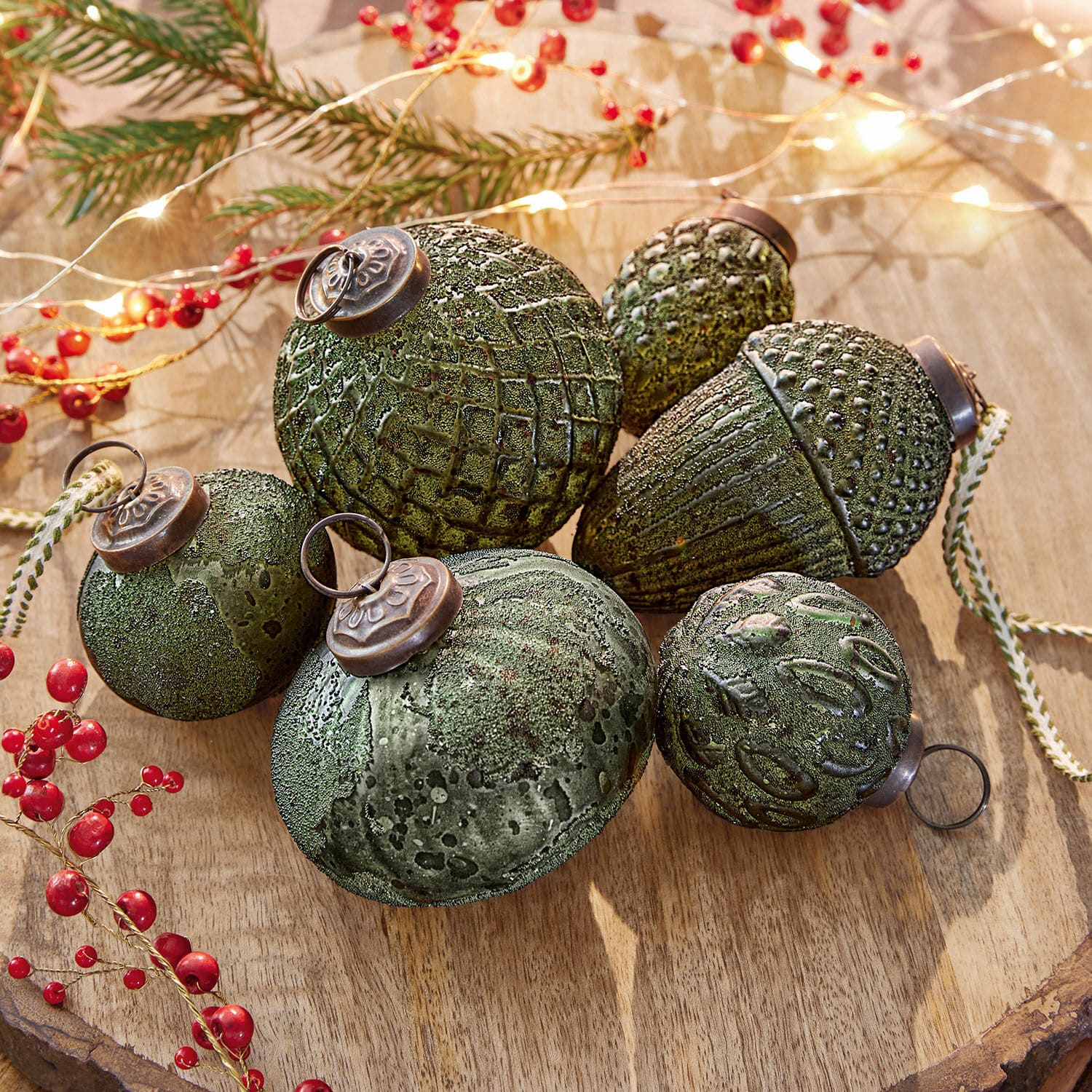 Set groene kerstballen met textuur en metalen ophangringen op houten ondergrond