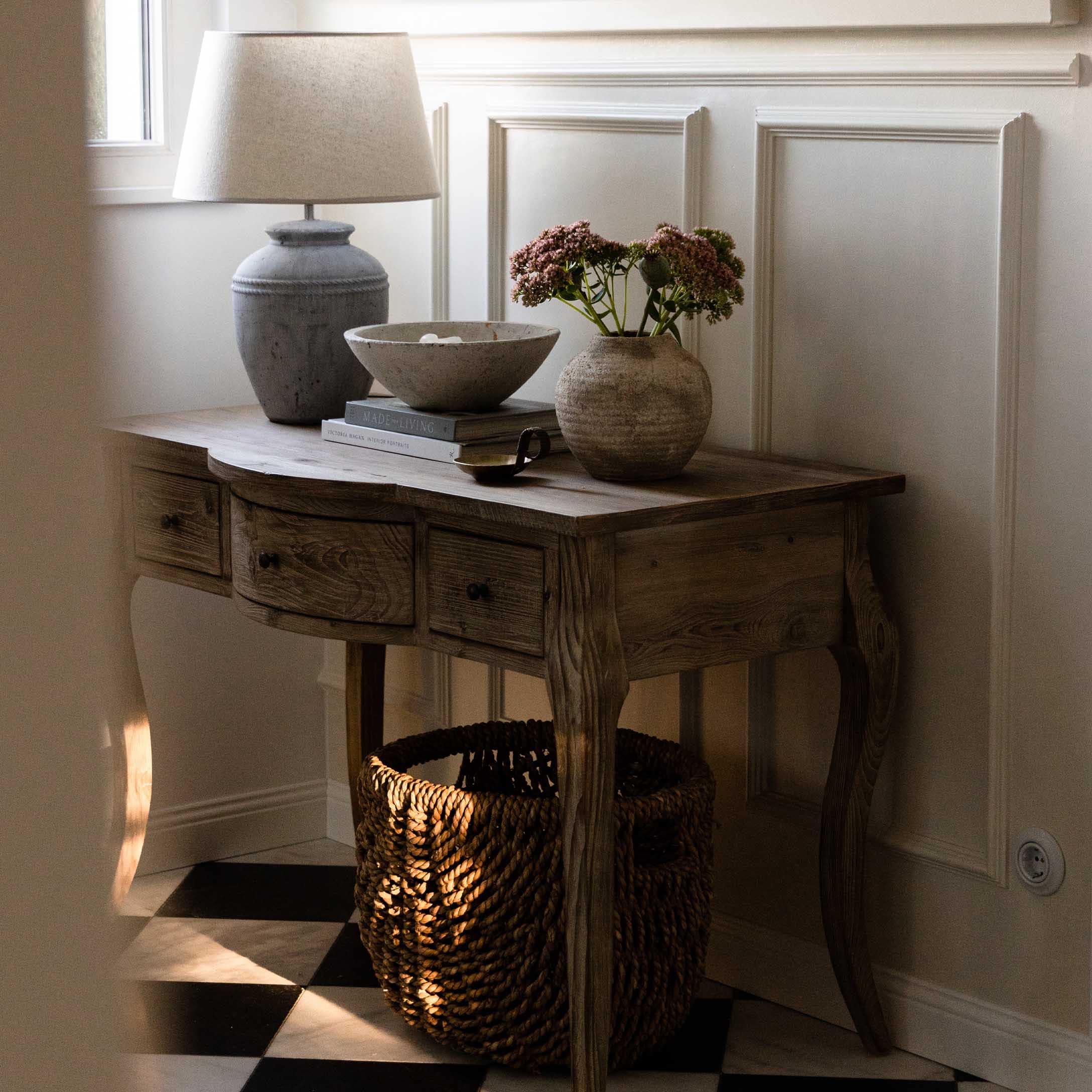 Houten tafel met lades, lamp, vaas en mand op zwart-witte dambordvloer