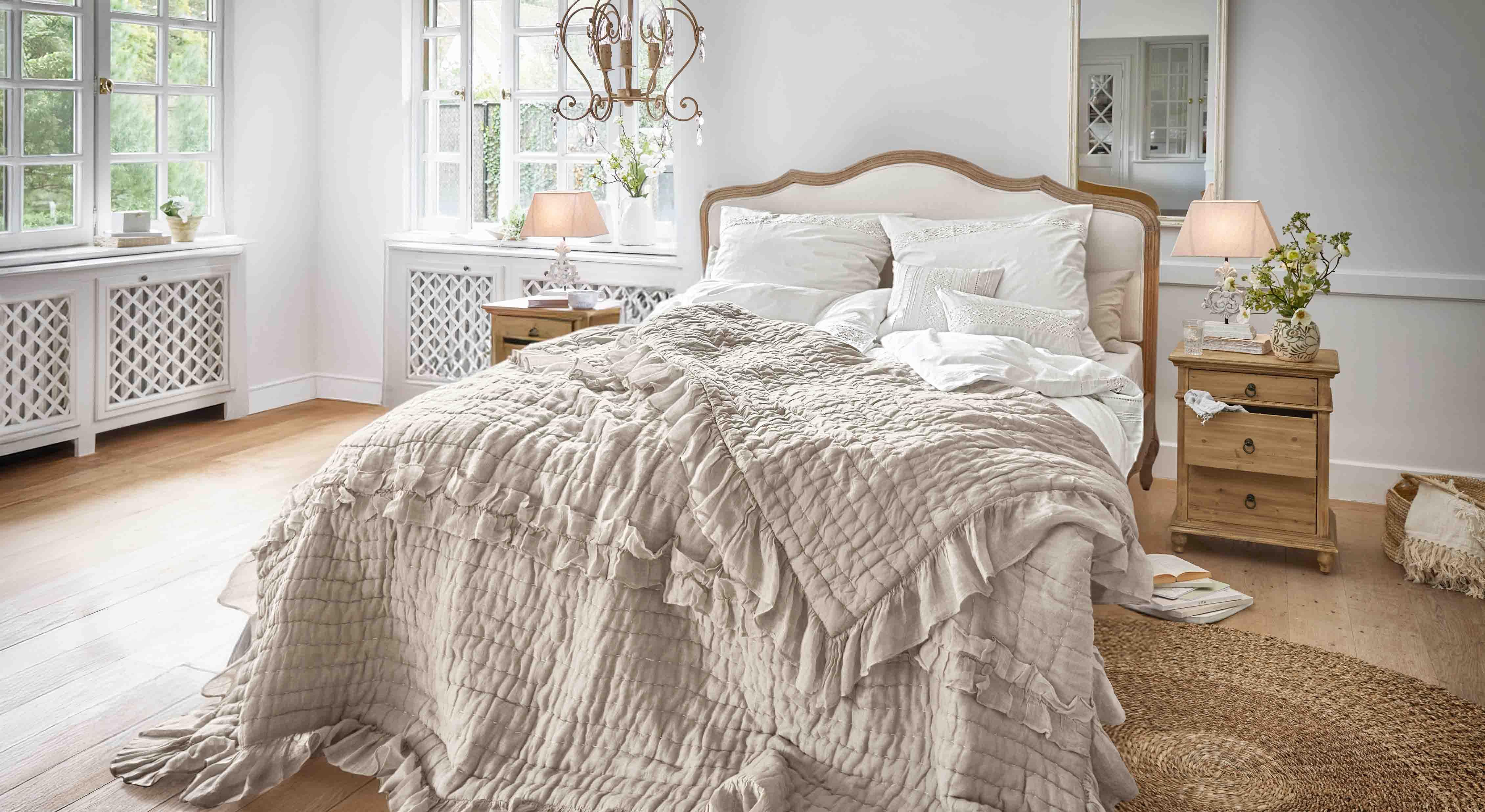 Gezellige slaapkamer met bed in beige sprei met ruches en lichte houten nachtkastjes