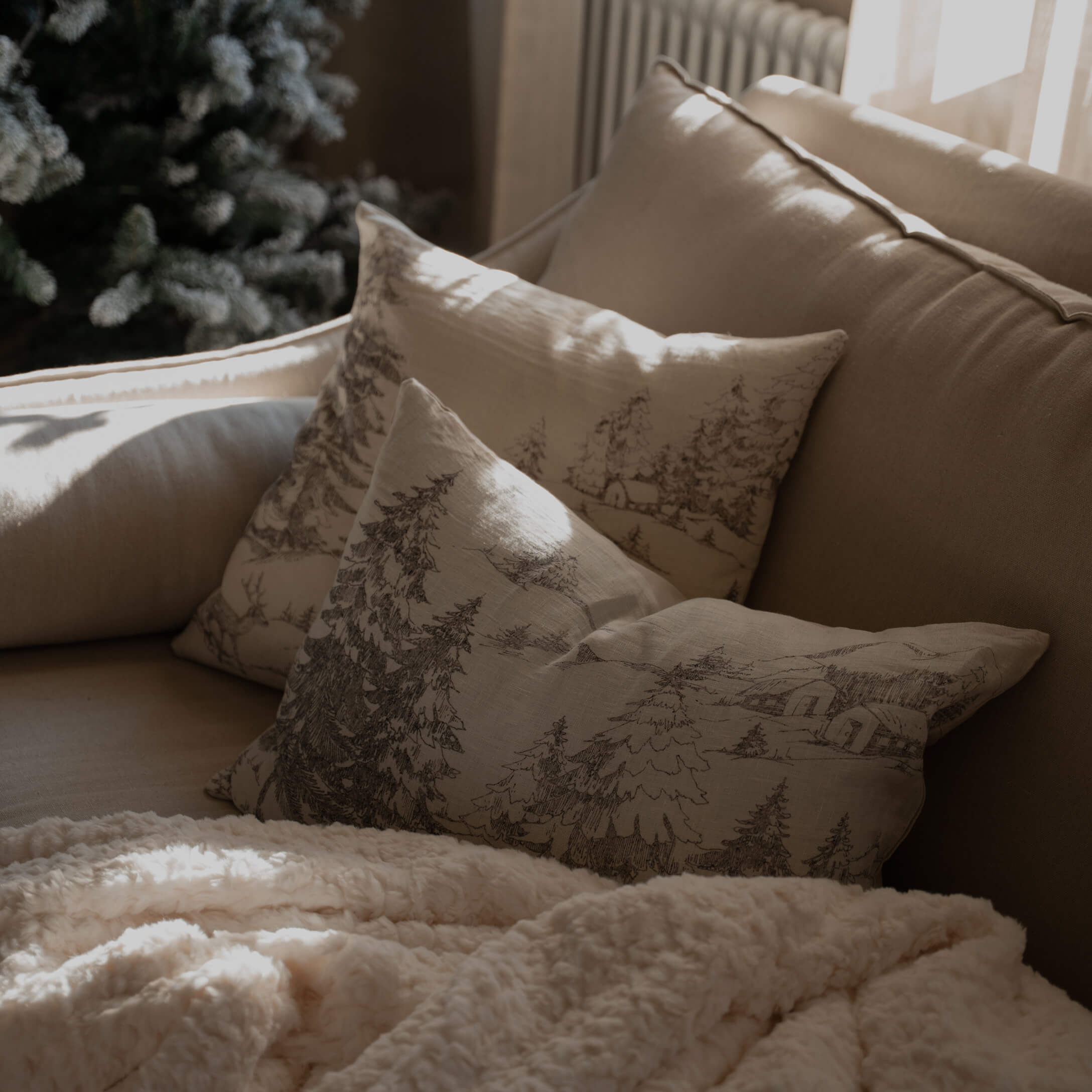 Beige bank met kussens met bosprint en zachte crèmekleurige deken voor een gezellige woonkamer