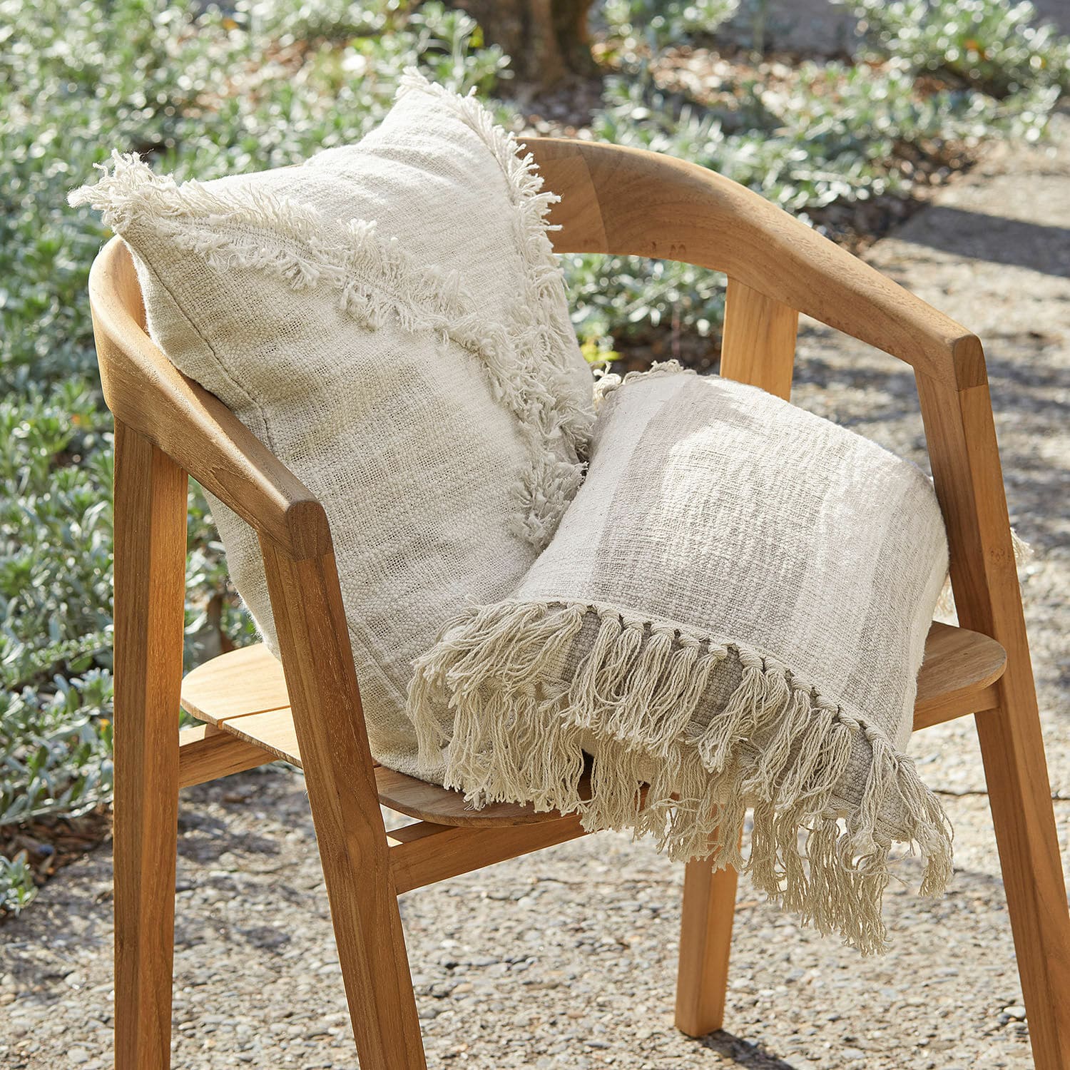 Beige katoenen kussen en deken met franjes op houten tuinstoel