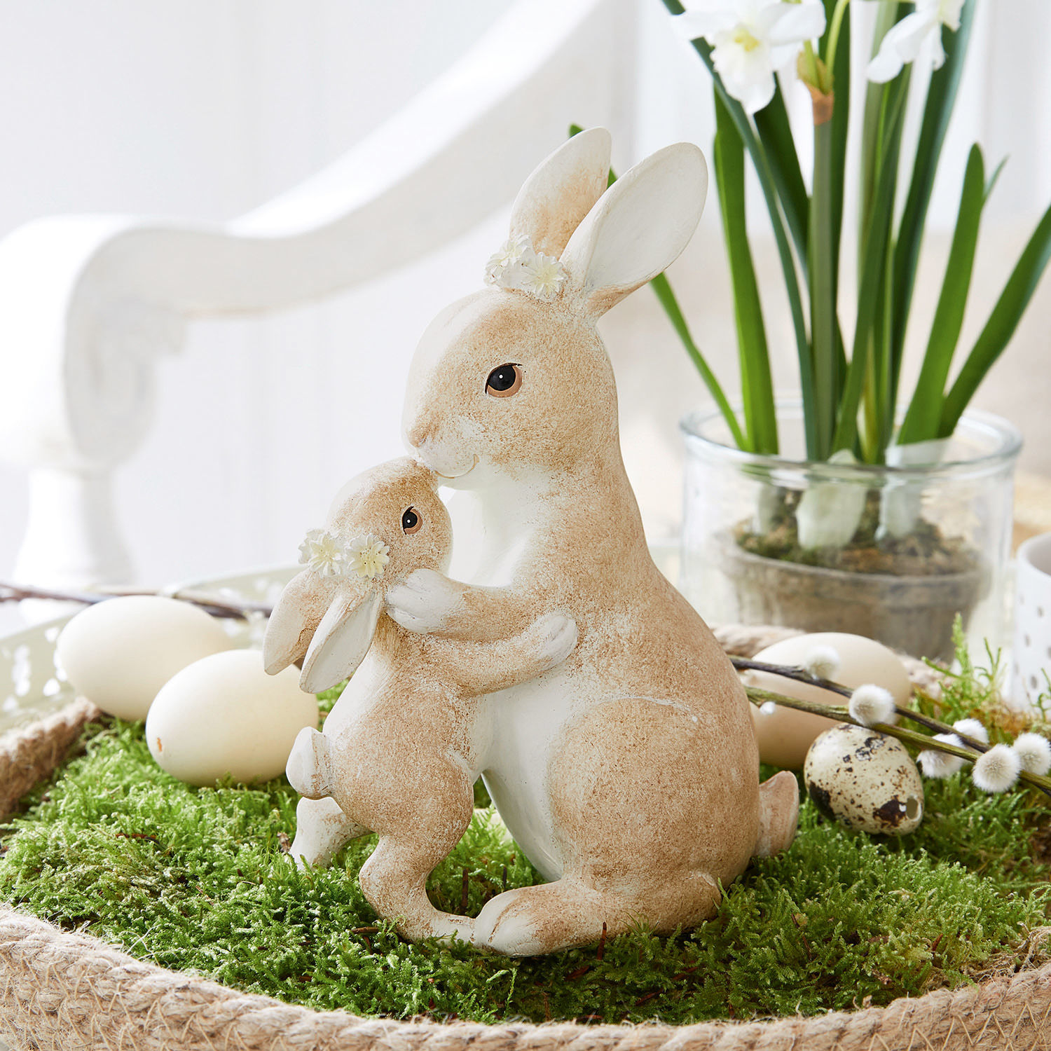 Hazen Aliena Beeldjes van twee beige-witte konijnen met bloemenkransen op groen mos, paasdecoratie