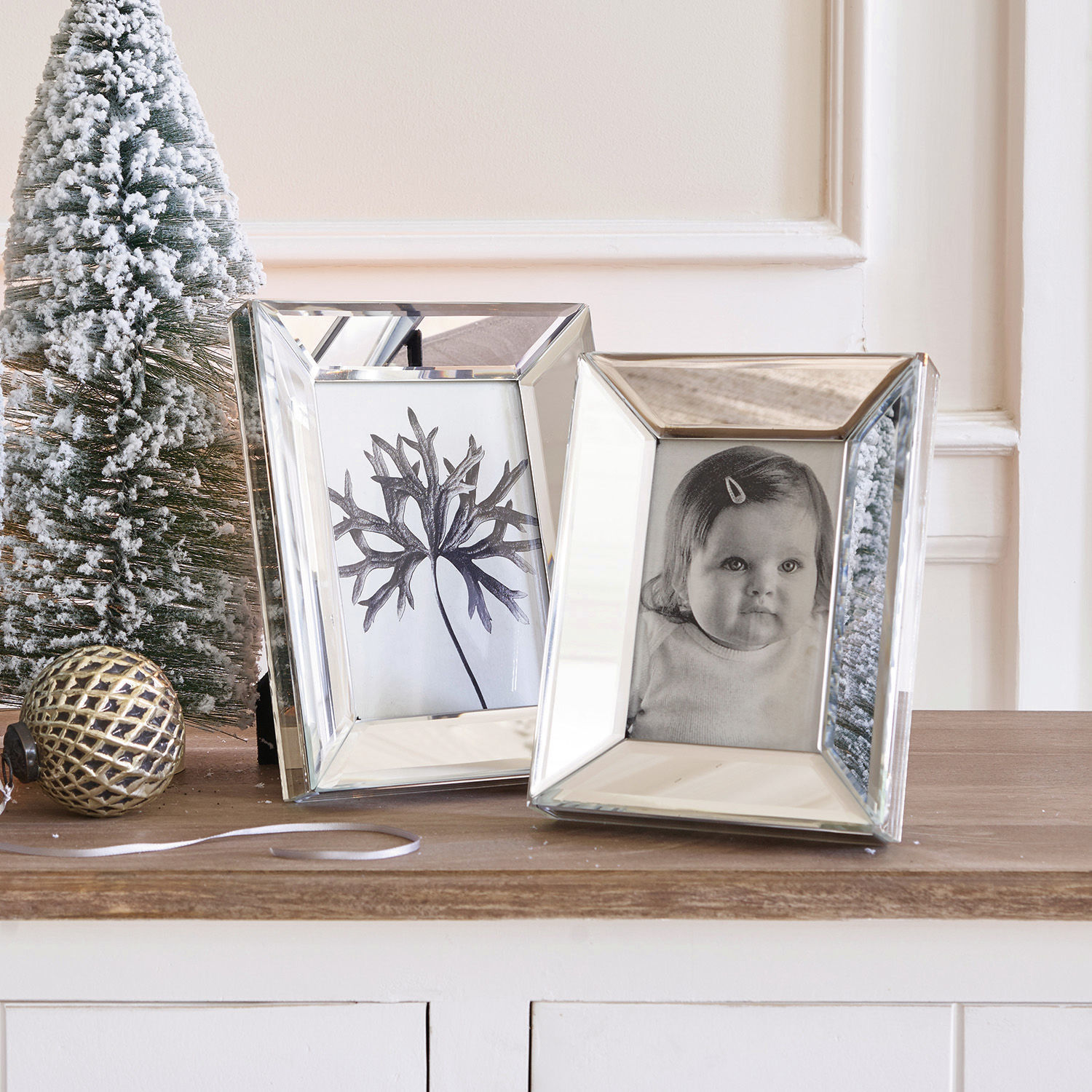 Twee spiegelende fotolijsten op houten tafel met kerstdecoratie en besneeuwde dennenboom