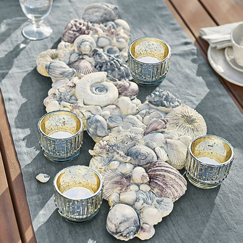 Decoratieve tafelloper met grijze schelpen en vier gouden glazen theelichthouders op houten tafel