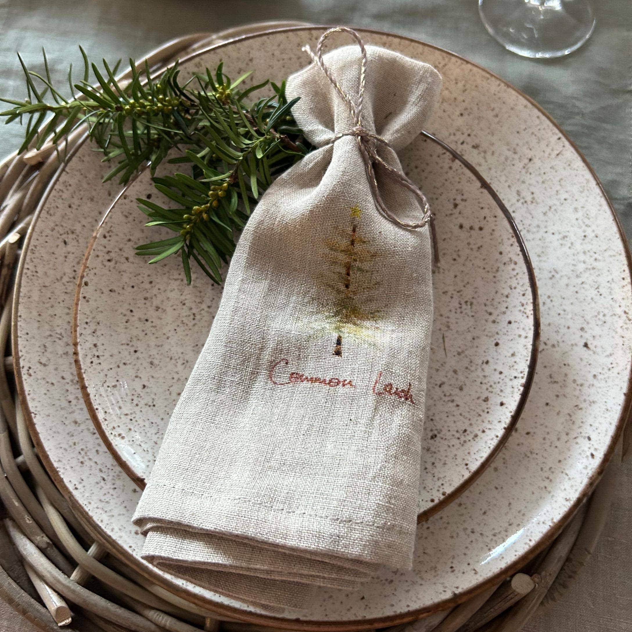 Beige linnen zakje met kerstboomprint op keramische bord met groene takken