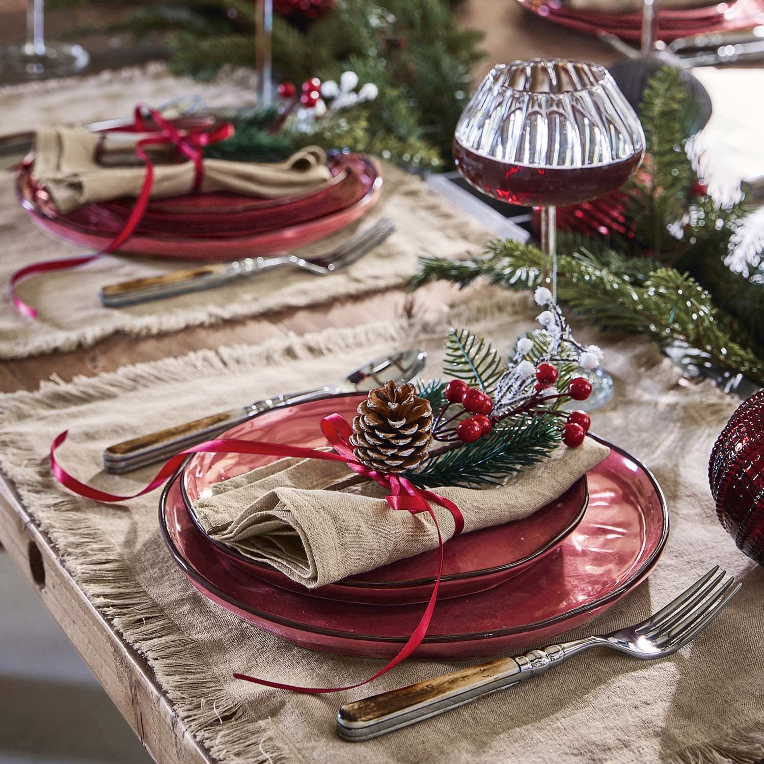 Feestelijk gedekte tafel met rode glazen borden en decoratie van dennenappel en rode bessen