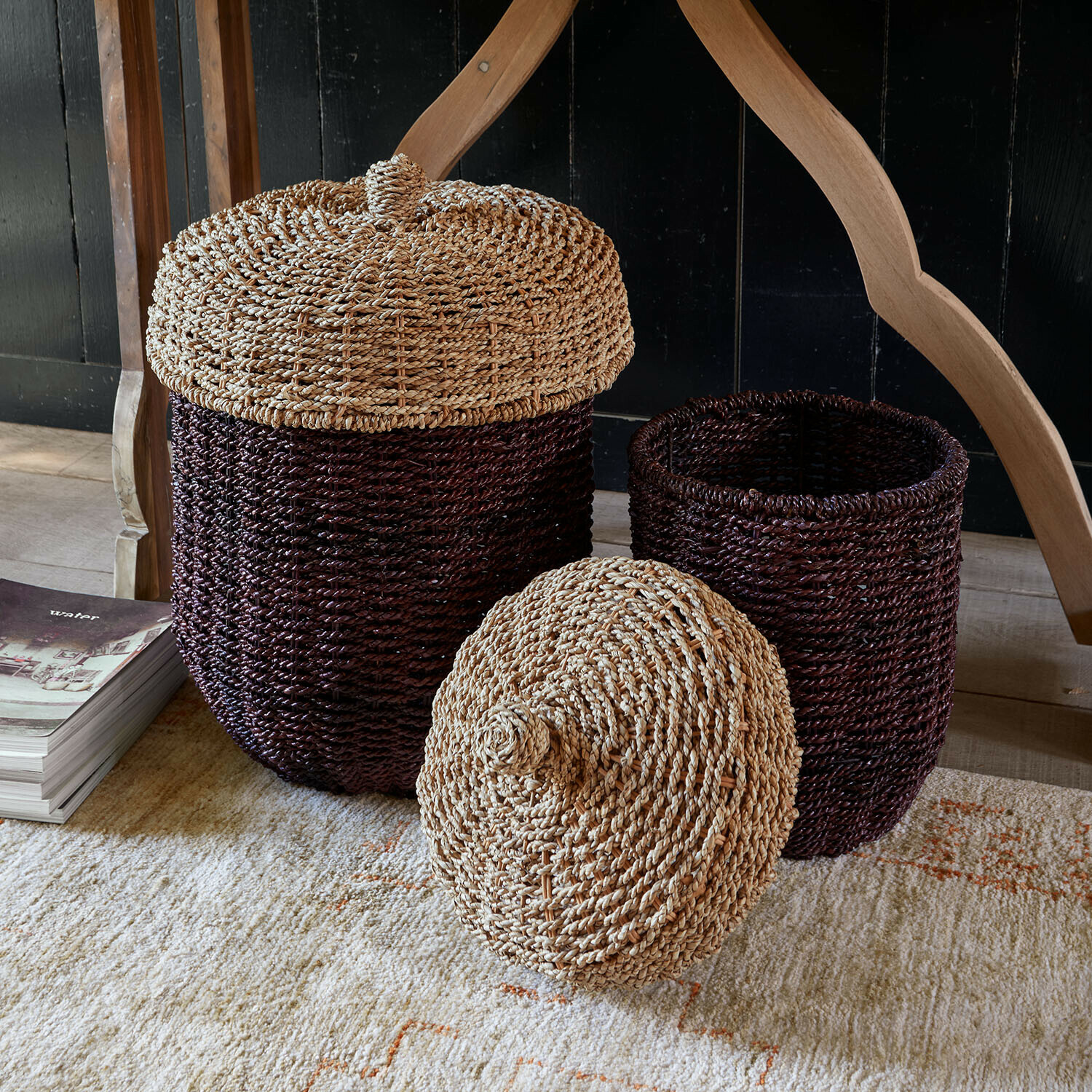 Mand set van 2 Aelwyn Set van twee bruine manden met deksels van gevlochten natuurlijk materiaal op een vloerkleed