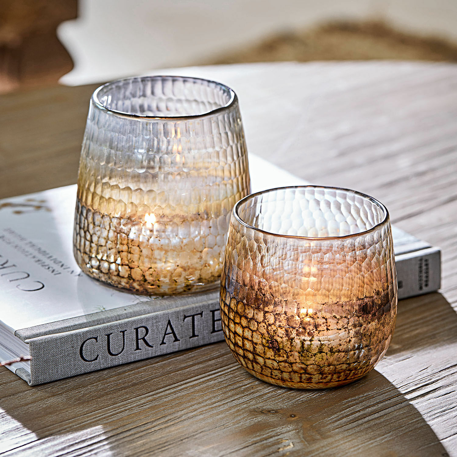 Twee gestructureerde glazen theelichthouders in bruine tinten op houten tafel met boek