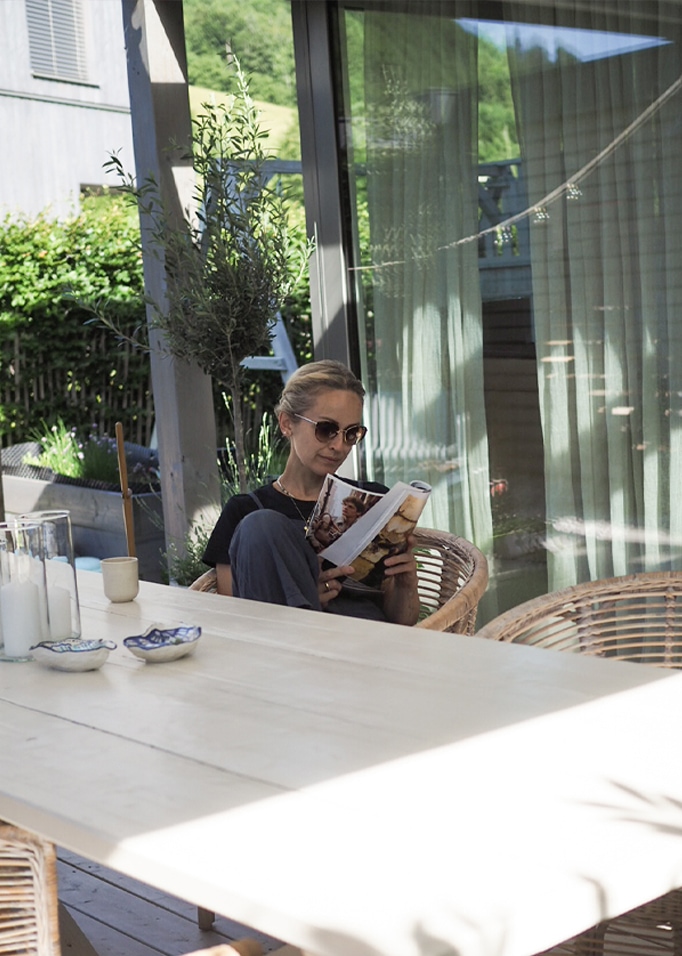 Vrouw leest boek op terras met rotan stoel en houten tafel op zonnige dag