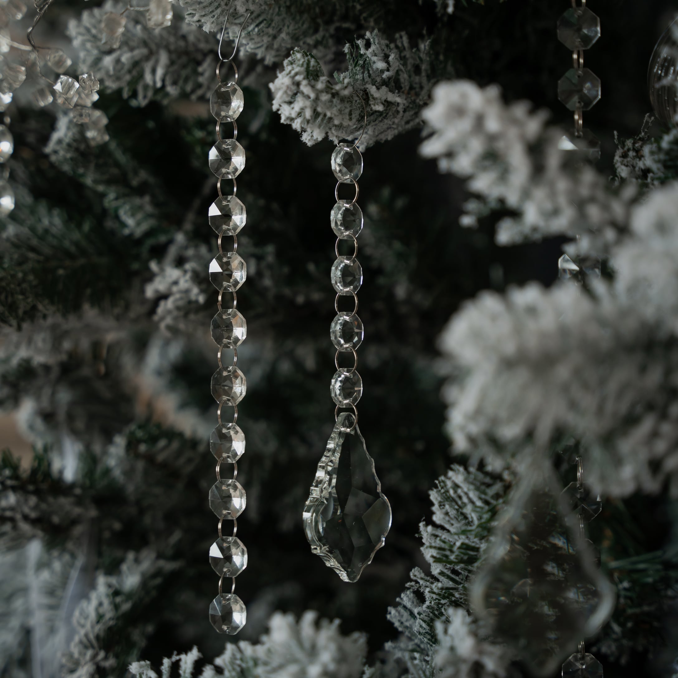 Kerstboomdecoratie van transparante kristallen kralen en hangers aan groene kunstboom met sneeuw effect