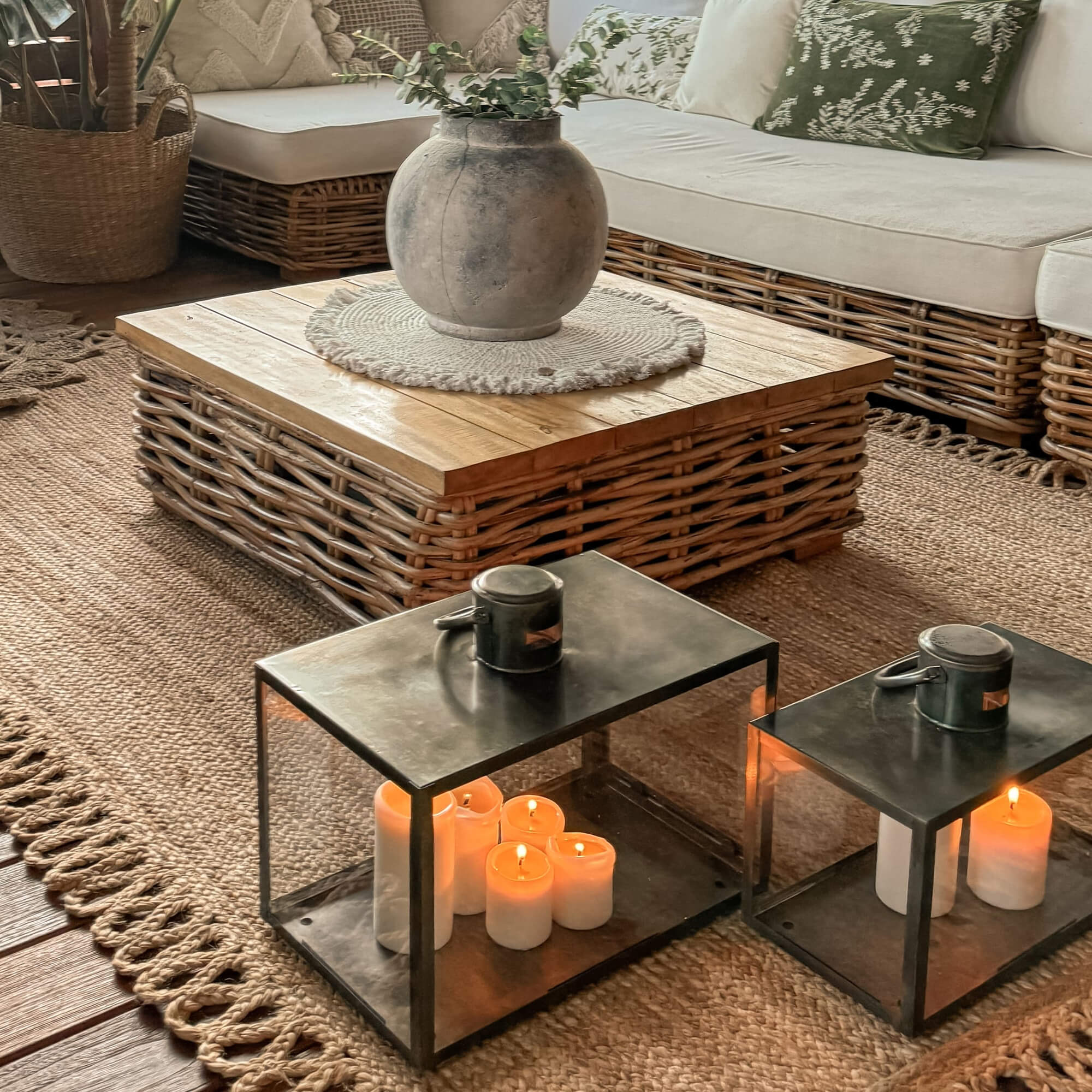 Metalen lantaarns met witte kaarsen op jute vloerkleed in gezellige woonkamer met rotan tafel