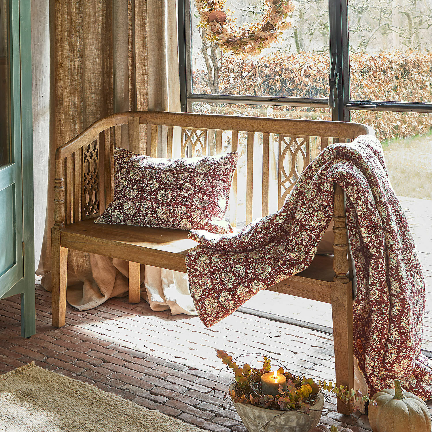 Houten bank met kussen en deken in bordeaux-crème bloemenpatroon in een gezellige ruimte