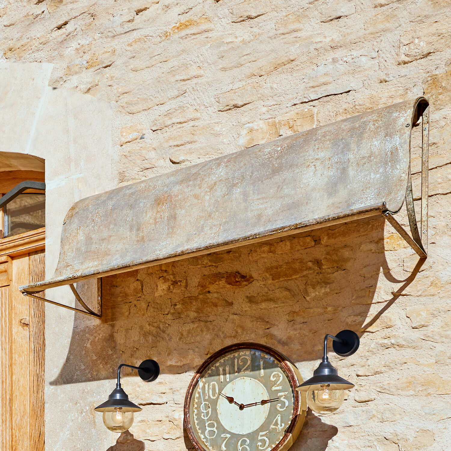Verweerde grijze metalen luifel aan stenen muur met klok en zwarte lampen