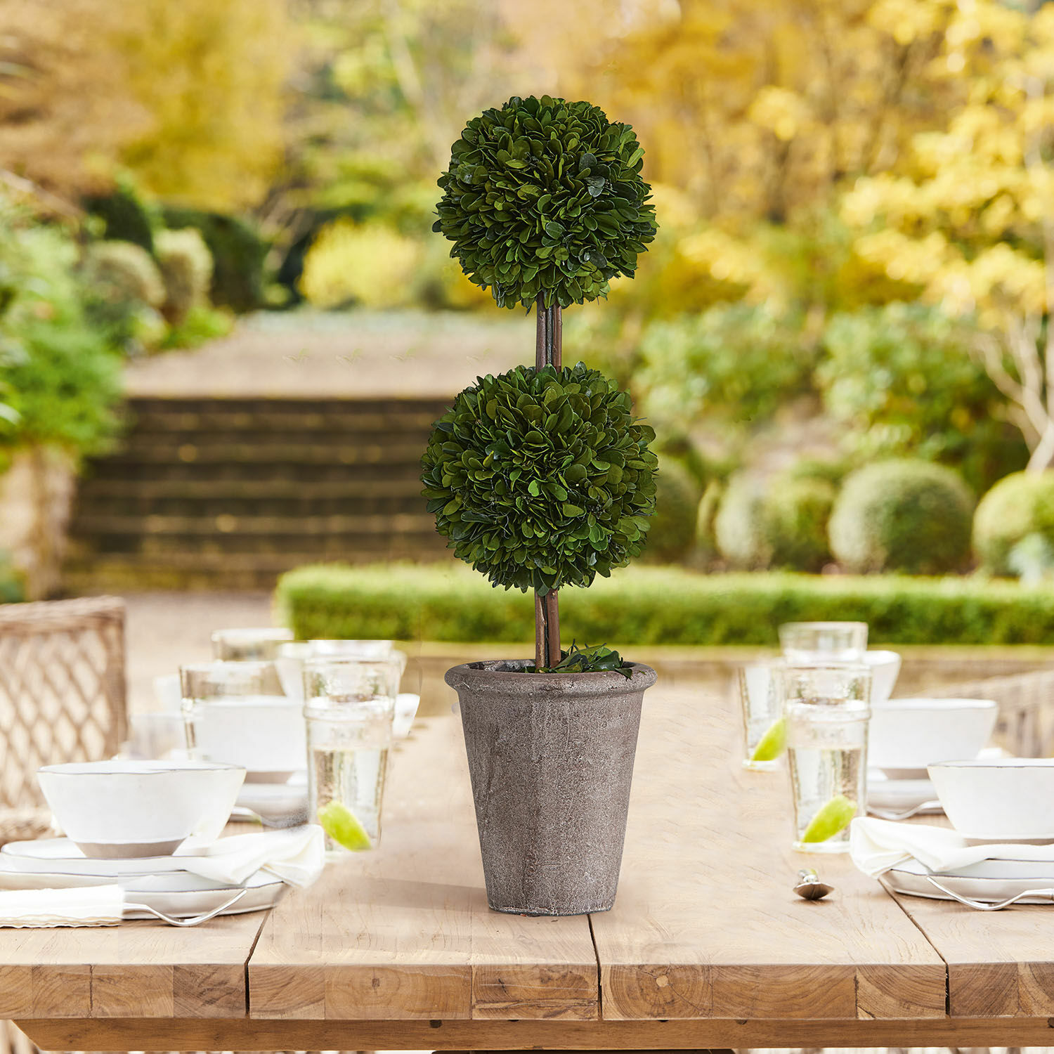 Decoratieve kunstplant in grijze stenen pot op houten tafel in tuin