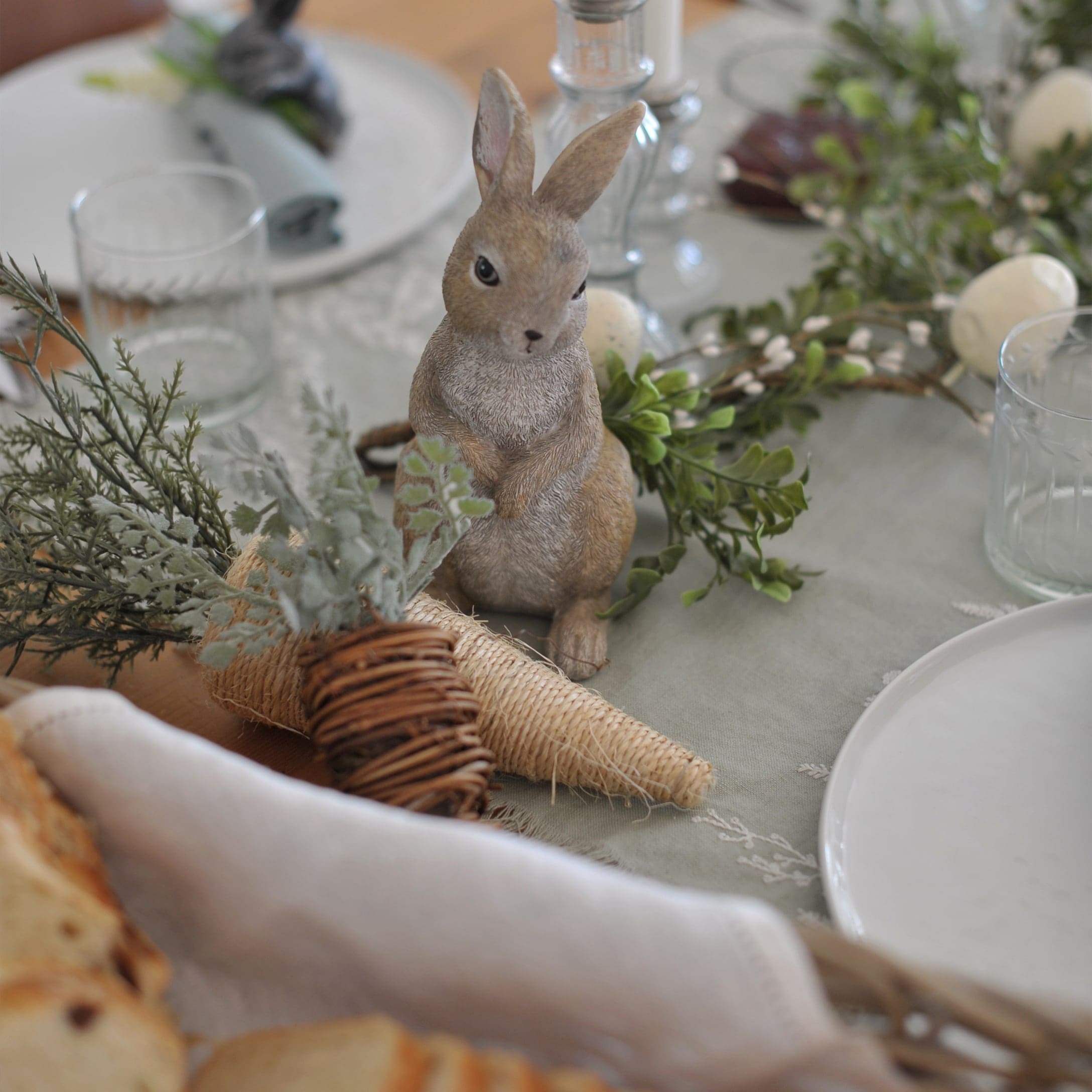 Decoratief konijn op tafel met natuurlijke versieringen en glas, lentetafel decoratie