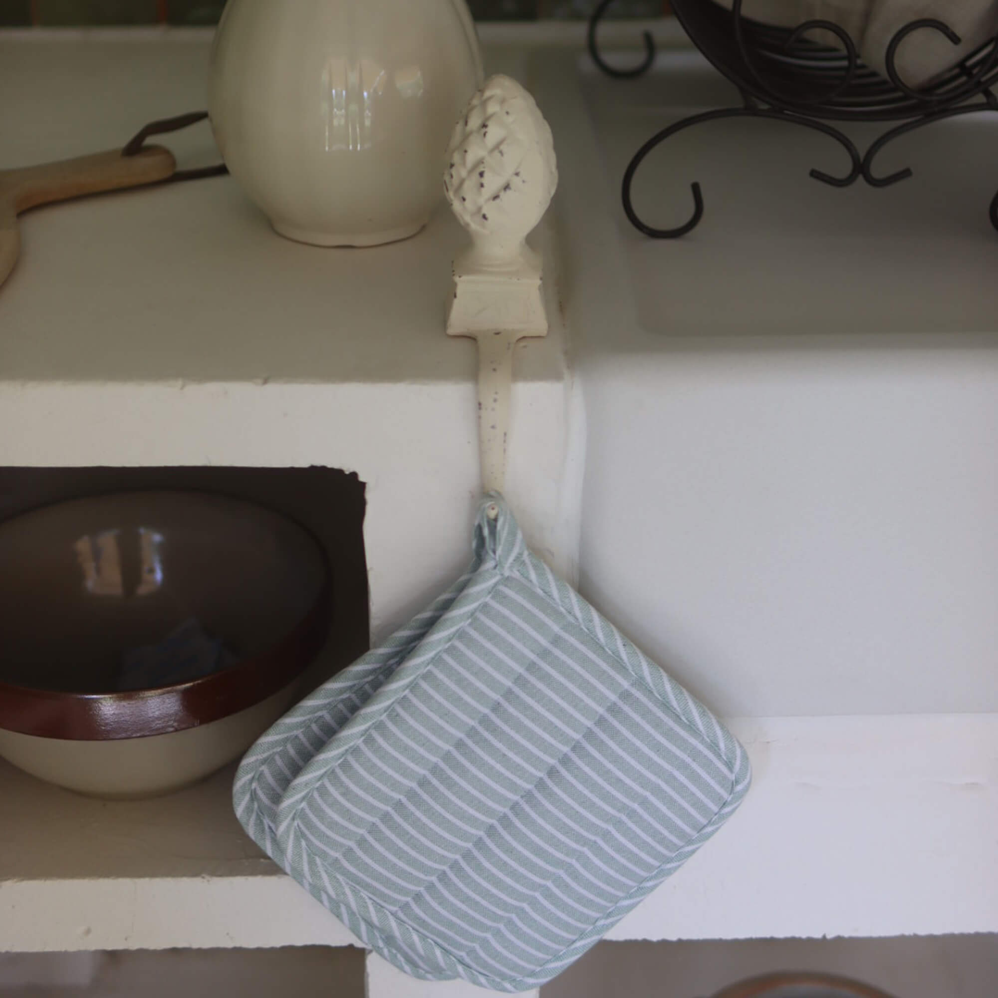 Mintgroene en witte katoenen gestreepte pannenlap hangend aan metalen haak in keuken