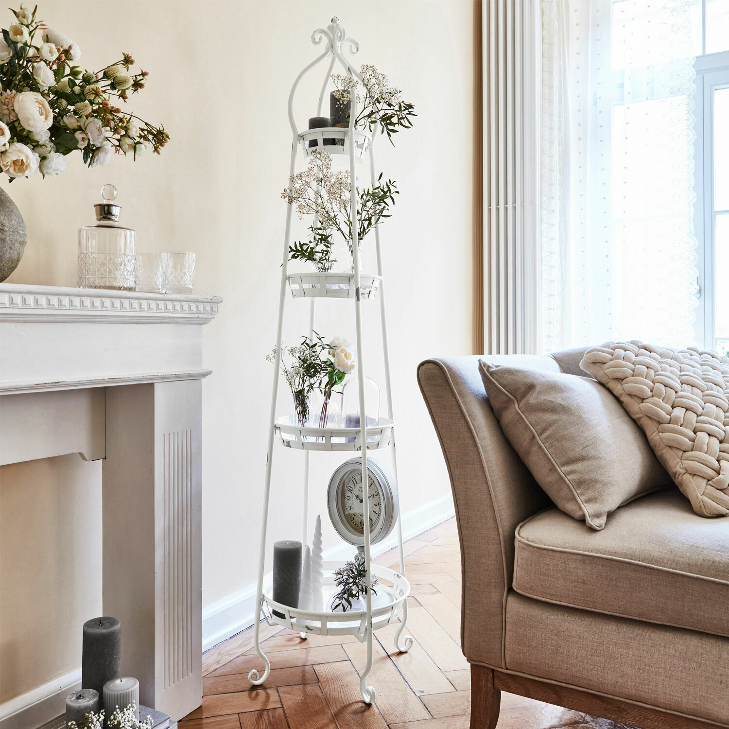 Witte metalen standaard met planken en bloemdecoraties in lichte woonkamer met beige bank