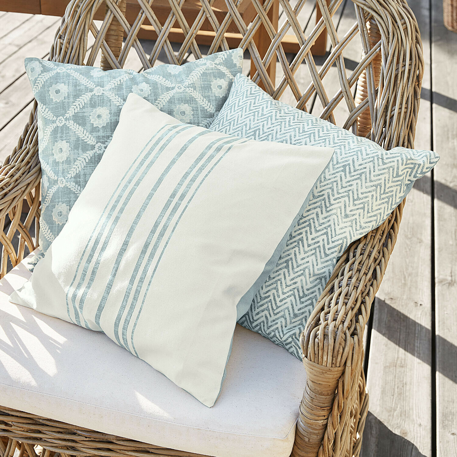 Kussenhoes set van 3 Sigruna Drie decoratieve kussens in blauw- en wit tinten op een rotan stoel op een houten terras