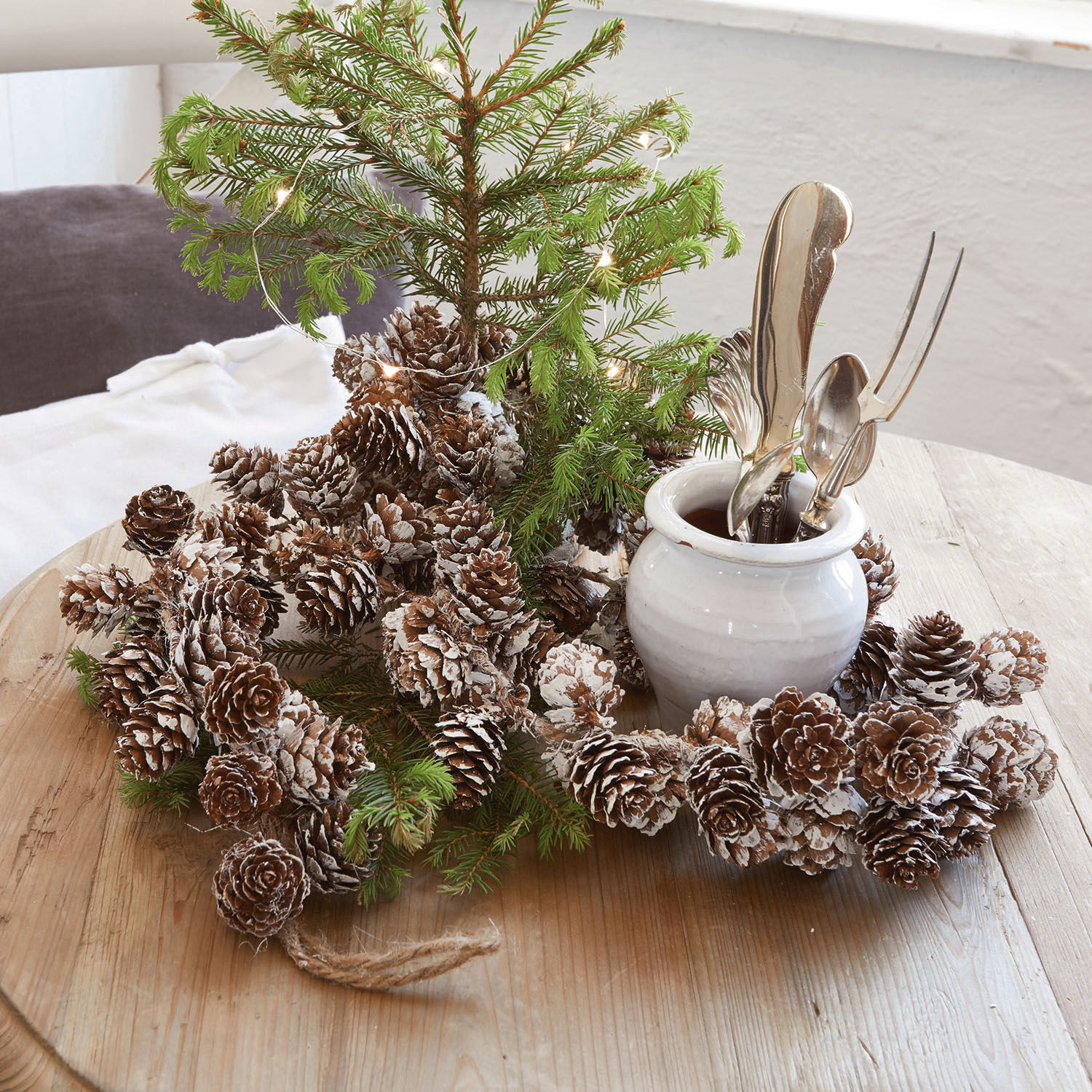 Guirlande Jacci Decoratieve dennenappelkrans met sneeuw effect op houten tafel met groene takken en witte vaas