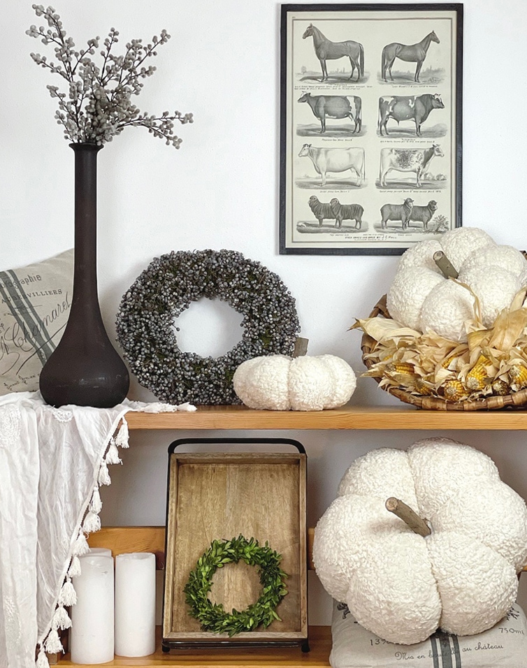 Herfstdecoratie met witte pluche pompoenen, groene kransen en zwarte vaas op houten plank