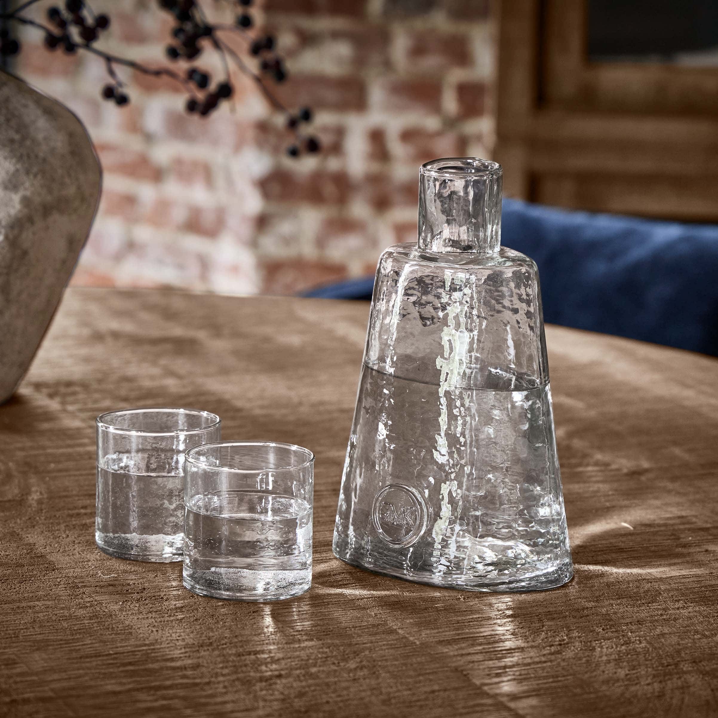 Transparante glazen karaf met twee glazen op houten tafel in rustieke omgeving