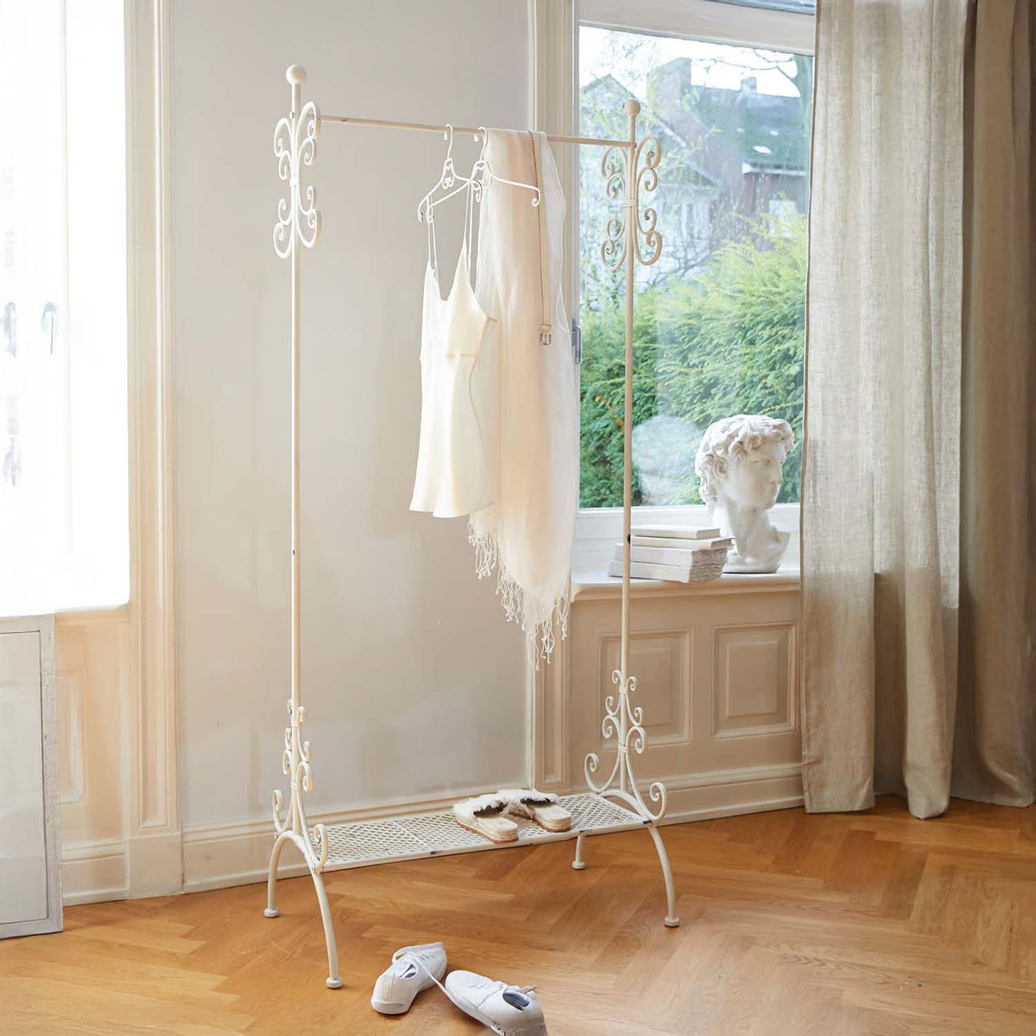 Witte metalen kledingrek met decoratieve details in lichte kamer met houten vloer