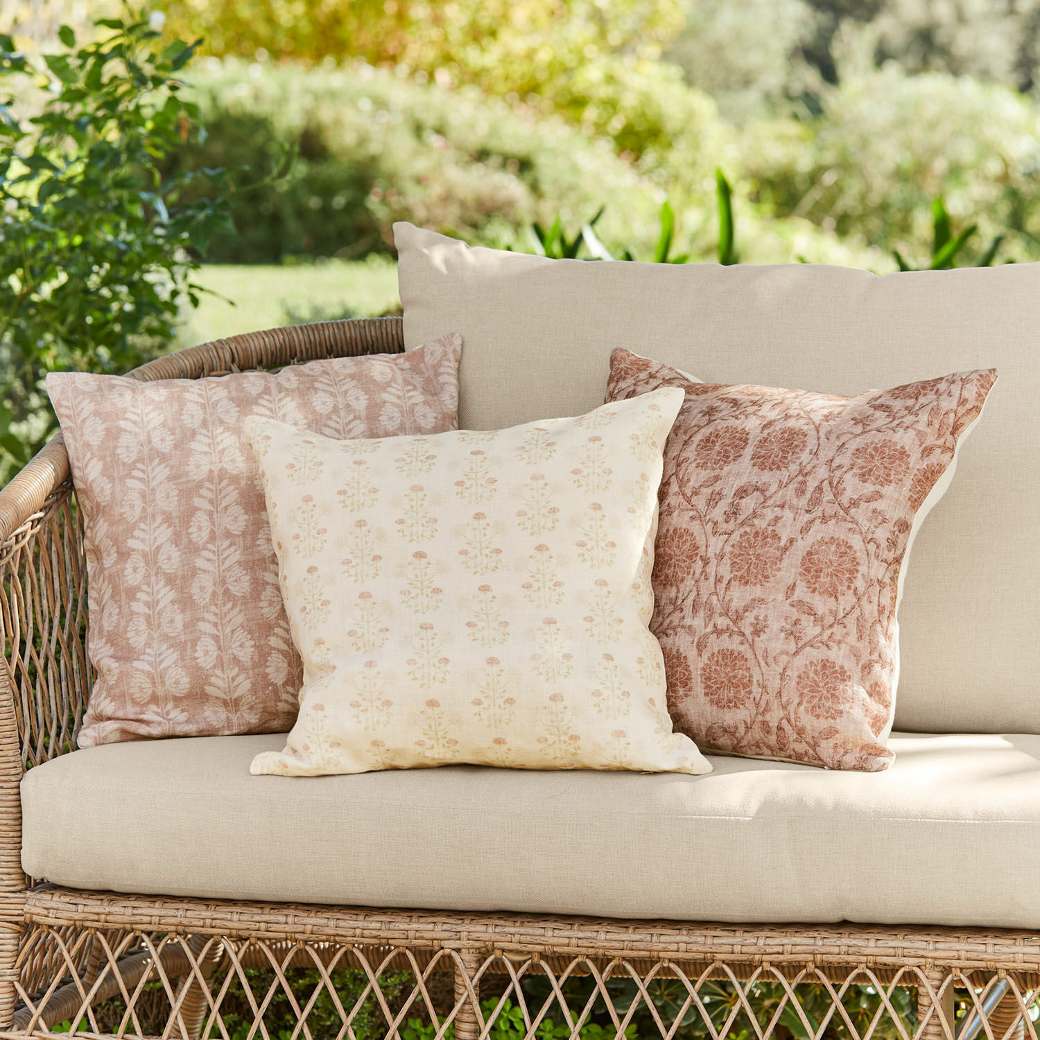 Set van drie decoratieve katoenen kussens in beige-roze patronen op een rotan tuinbank