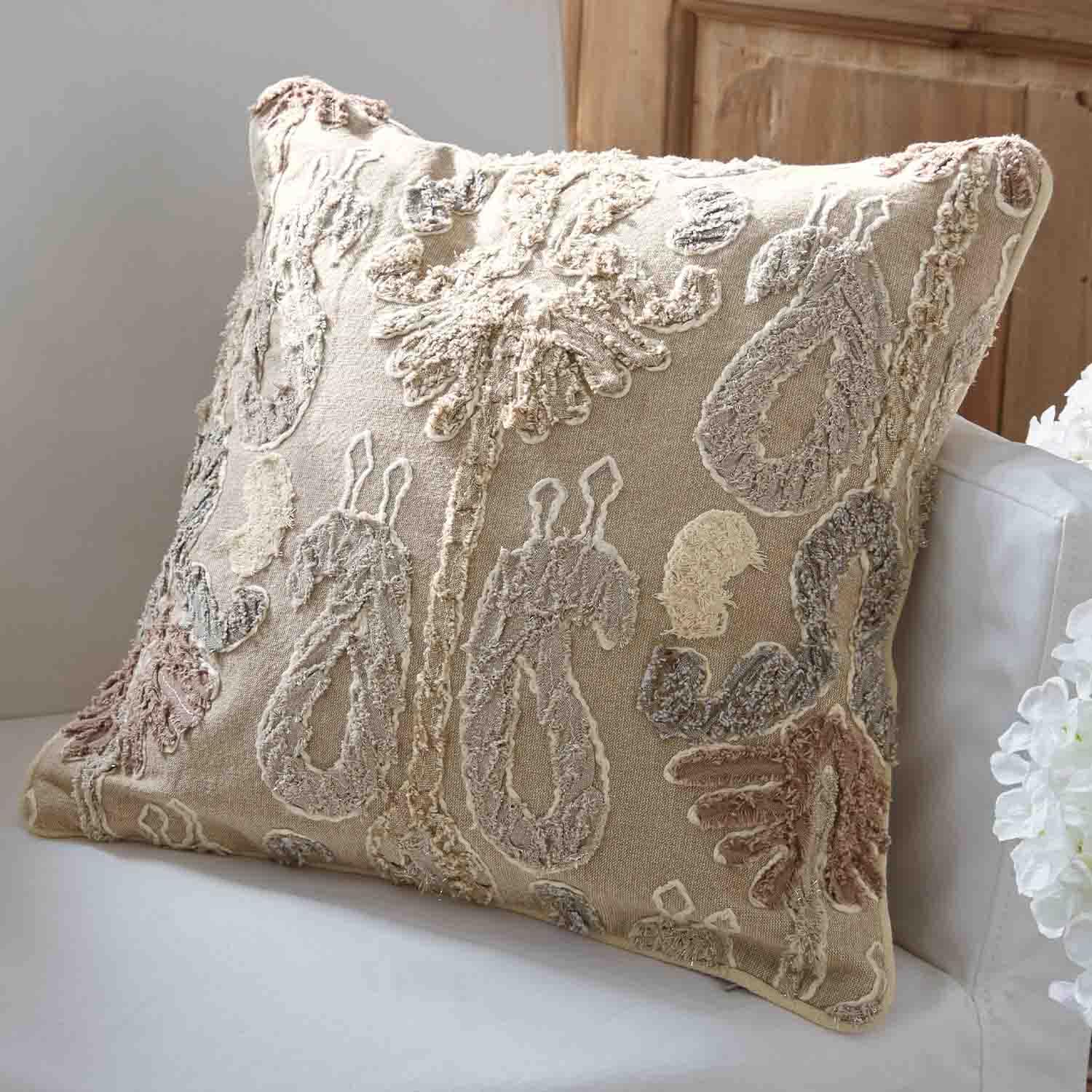 Beige sierkussen met geborduurd patroon in pasteltinten op een witte bank