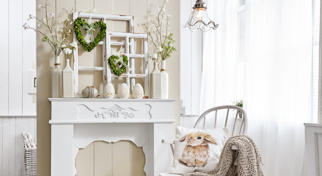 Witte decoratieve schoorsteen met groene hartkransen en konijnenkussen in lichte kamer