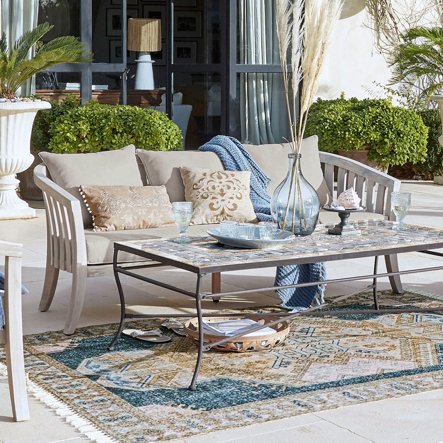 Bank Seanad Beige houten loungesofa met kussens en metalen tafel met mozaïekblad op terras