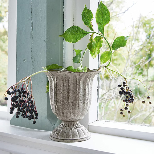 Grijze keramische decoratieve vaas met groene bladeren en zwarte bessen op vensterbank
