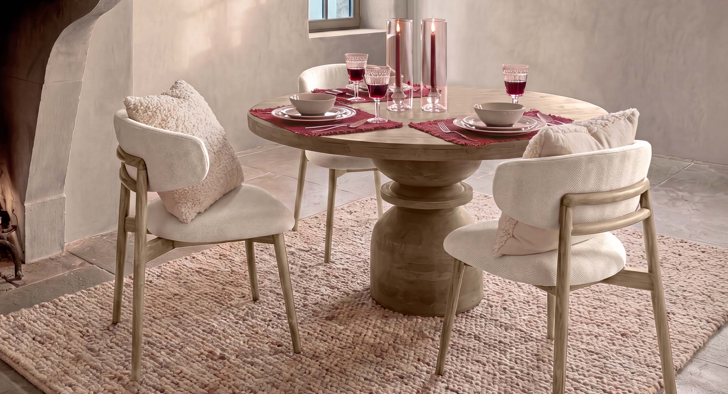 Lichte houten ronde tafel met crèmekleurige stoelen en kussens op een zachte vloerkleed in eetkamer