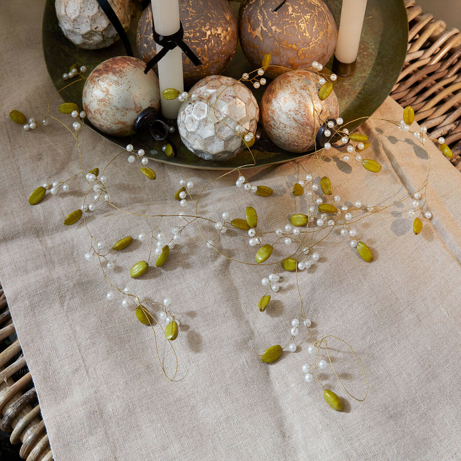 Guirlande Kelira Decoratieve slinger met groene en witte kralen op linnen tafelkleed met decoratieve ballen