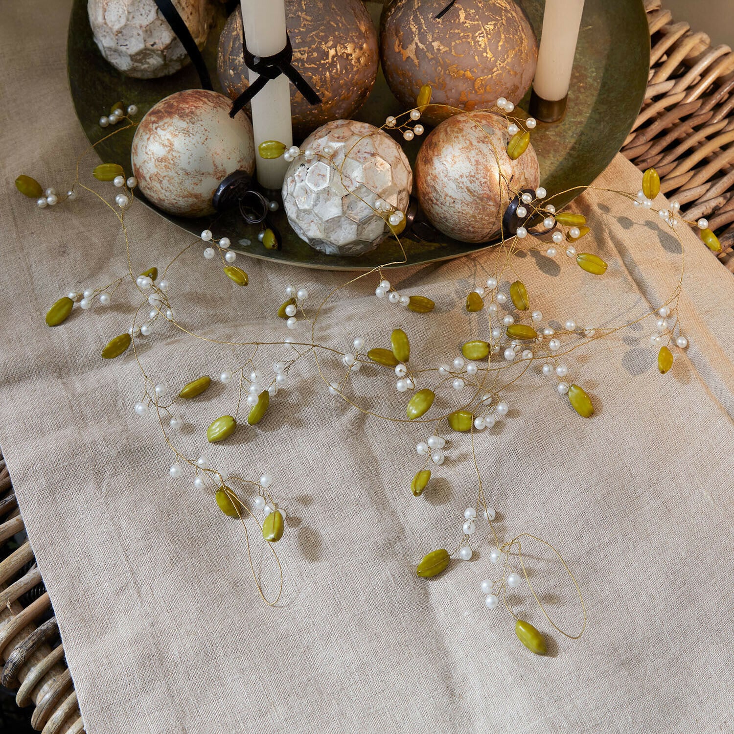 Guirlande Kelira Decoratieve slinger met groene en witte kralen op linnen tafelkleed met decoratieve ballen