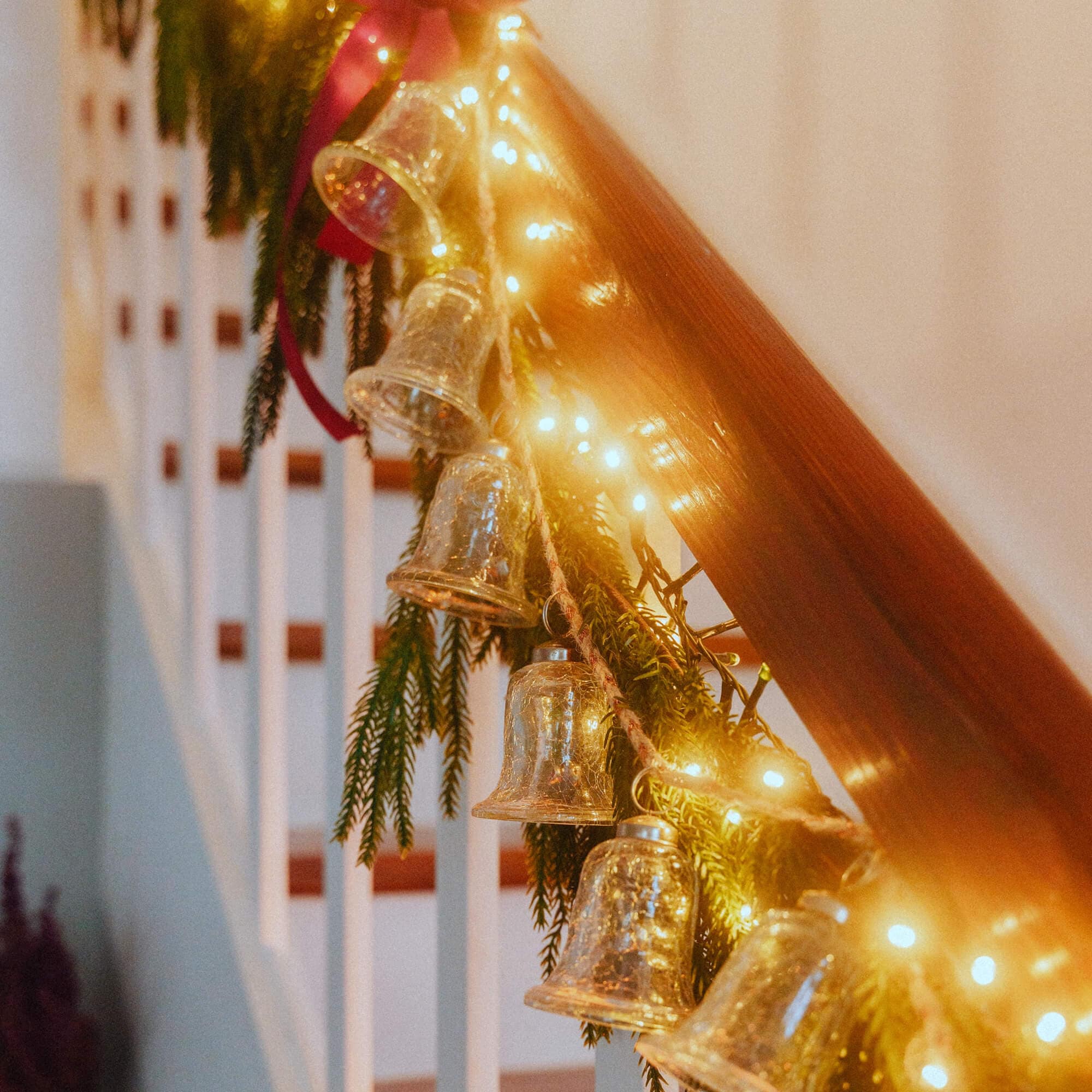 Glazen belletjes en LED-lichtjes aan houten trapleuning met groene takken als decoratie