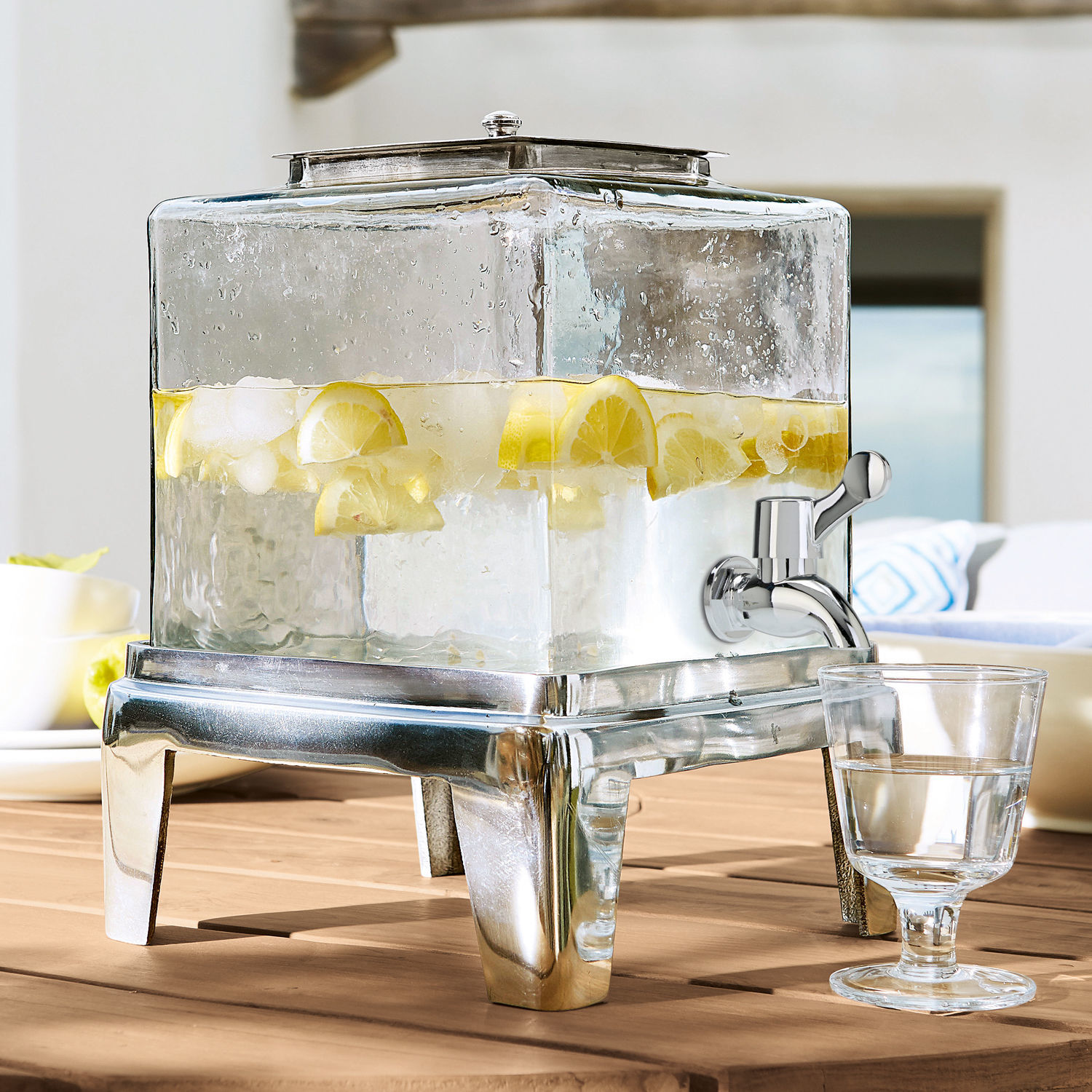 Glazen drankendispenser met metalen voet en kraan, gevuld met water en citroen
