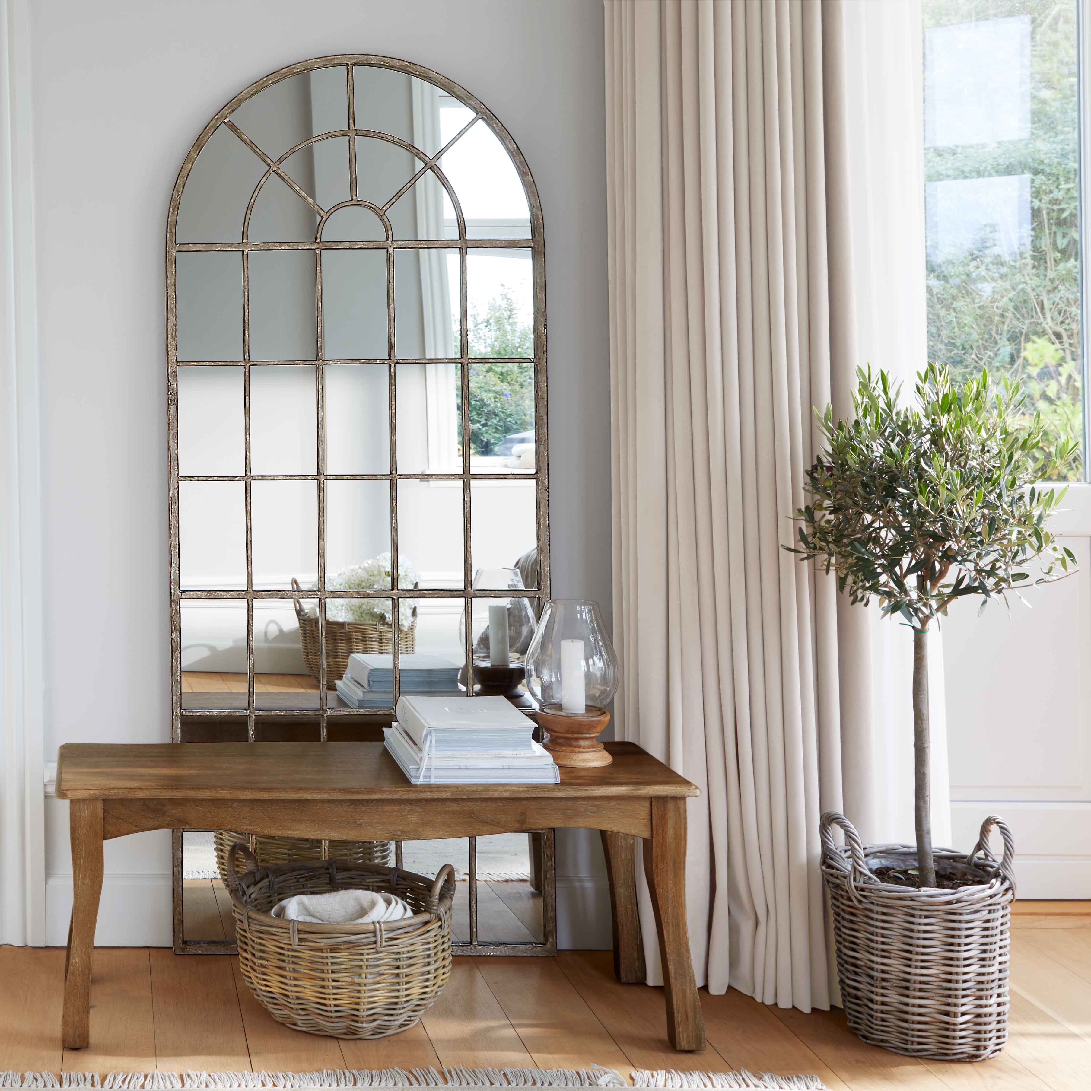 Houten tafel met metalen lijst spiegel en rieten mand in lichte kamer met gordijnen