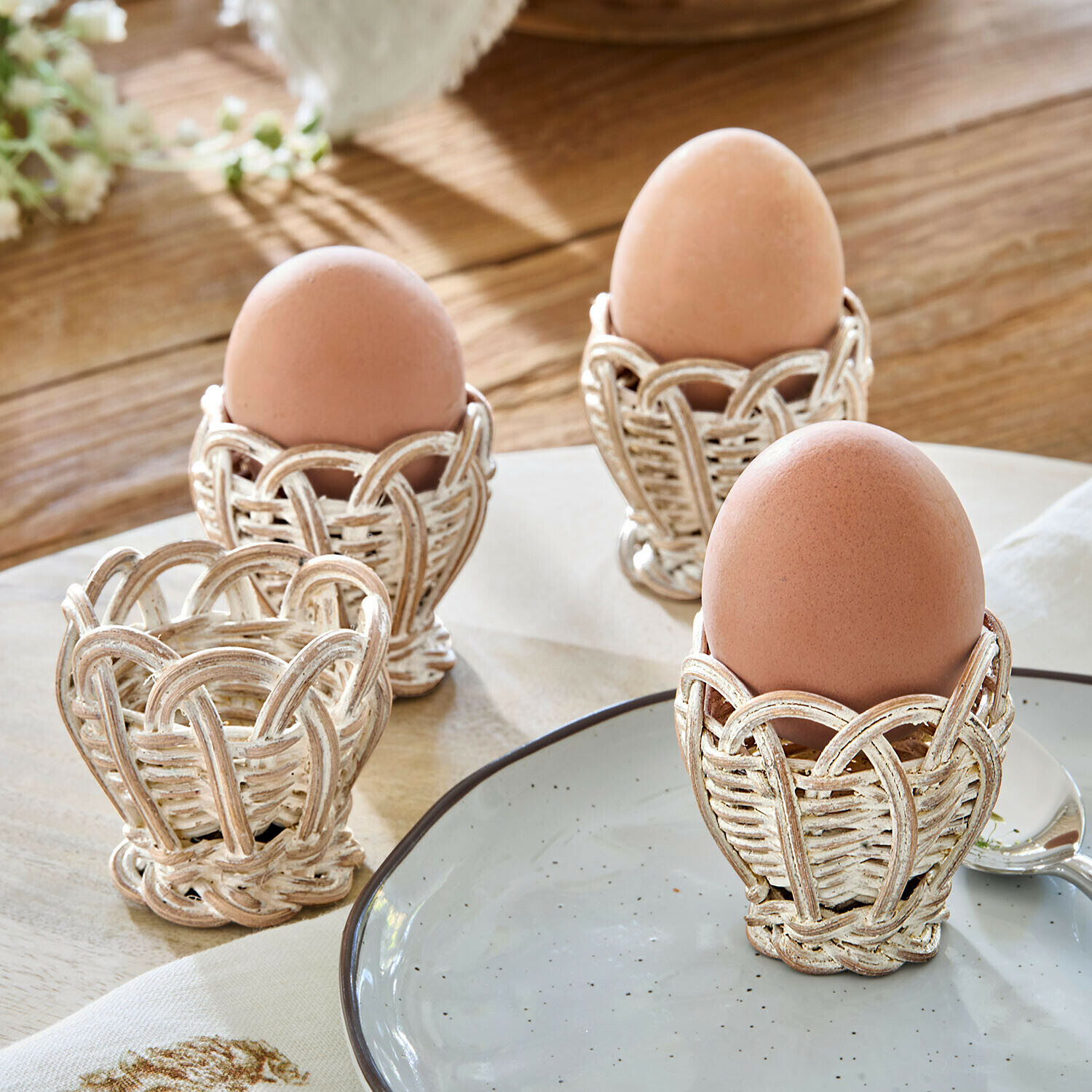 Eierdopje set van 4 Minouvelle Set van vier witte verweerde rieten eierdopjes op houten tafel, rustieke stijl