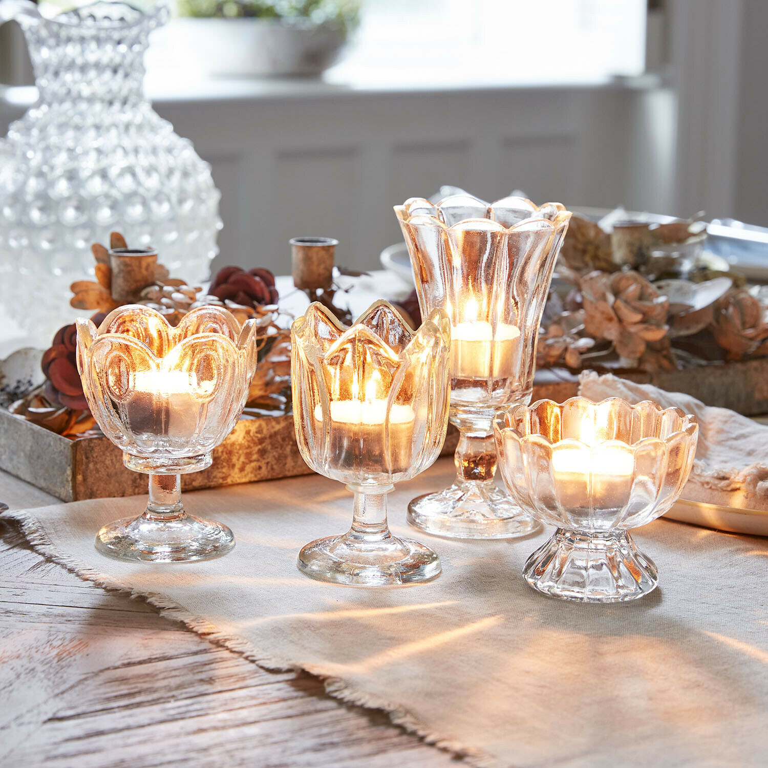 Vier transparante glazen theelichthouders op voet met brandende kaarsen, tafeldecoratie