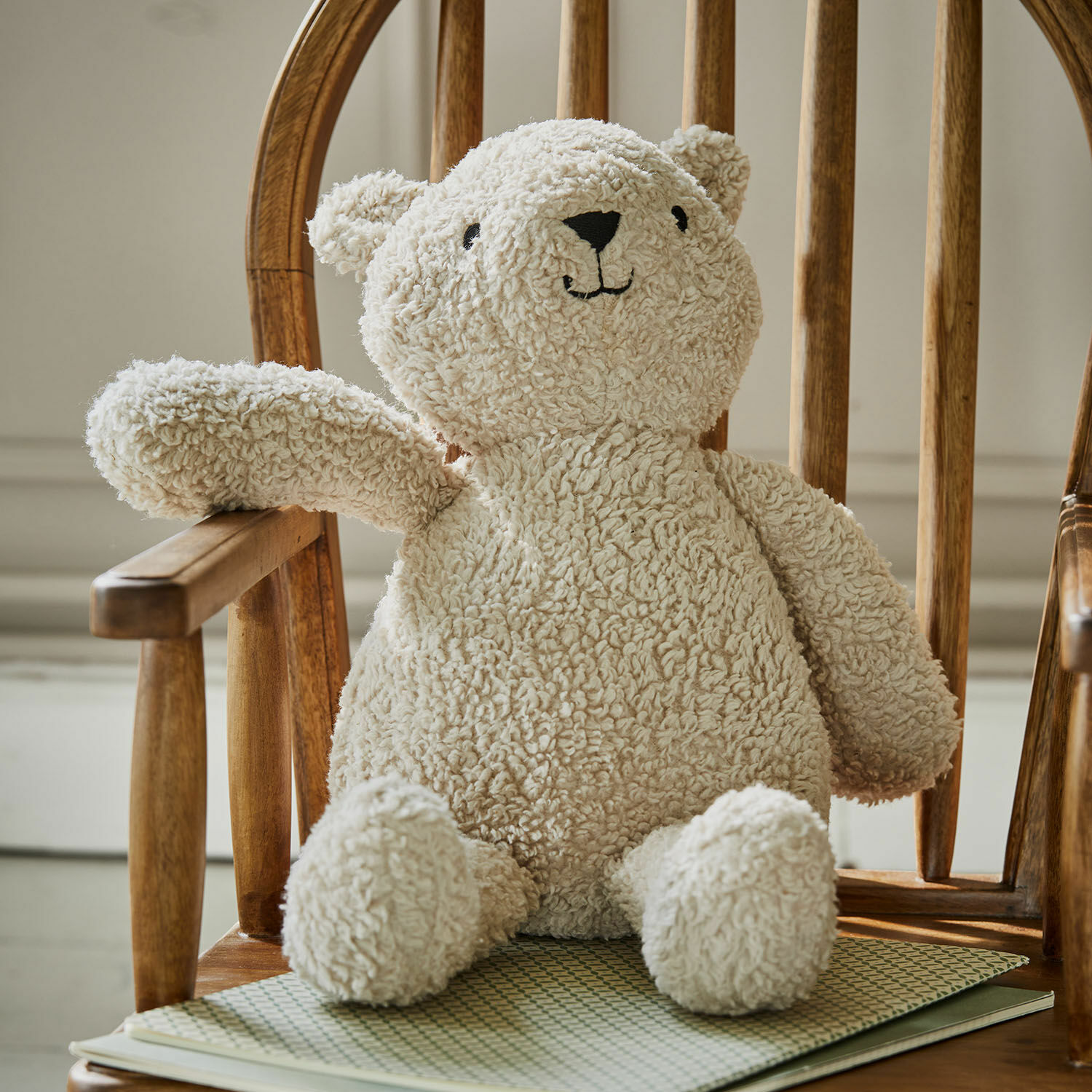 Knuffeltje Fuffino Knuffelbeer van zacht crèmekleurig materiaal op houten stoel, kinderkamerdecoratie