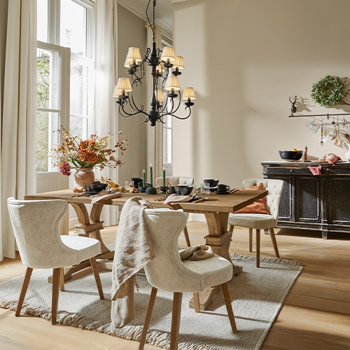 Eetkamer met houten tafel, crèmekleurige gestoffeerde stoelen, bloemen en zwarte kroonluchter