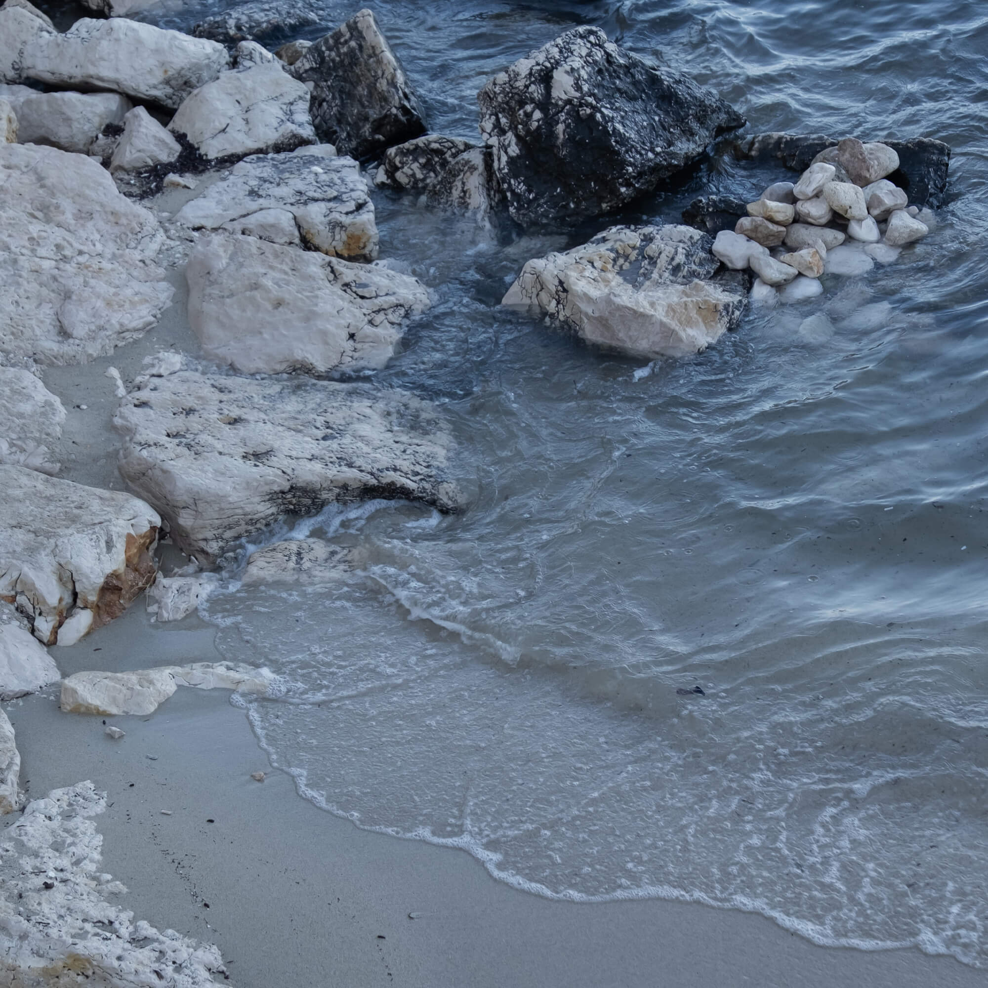 Kust met lichte en donkere stenen en golven die op het zand breken